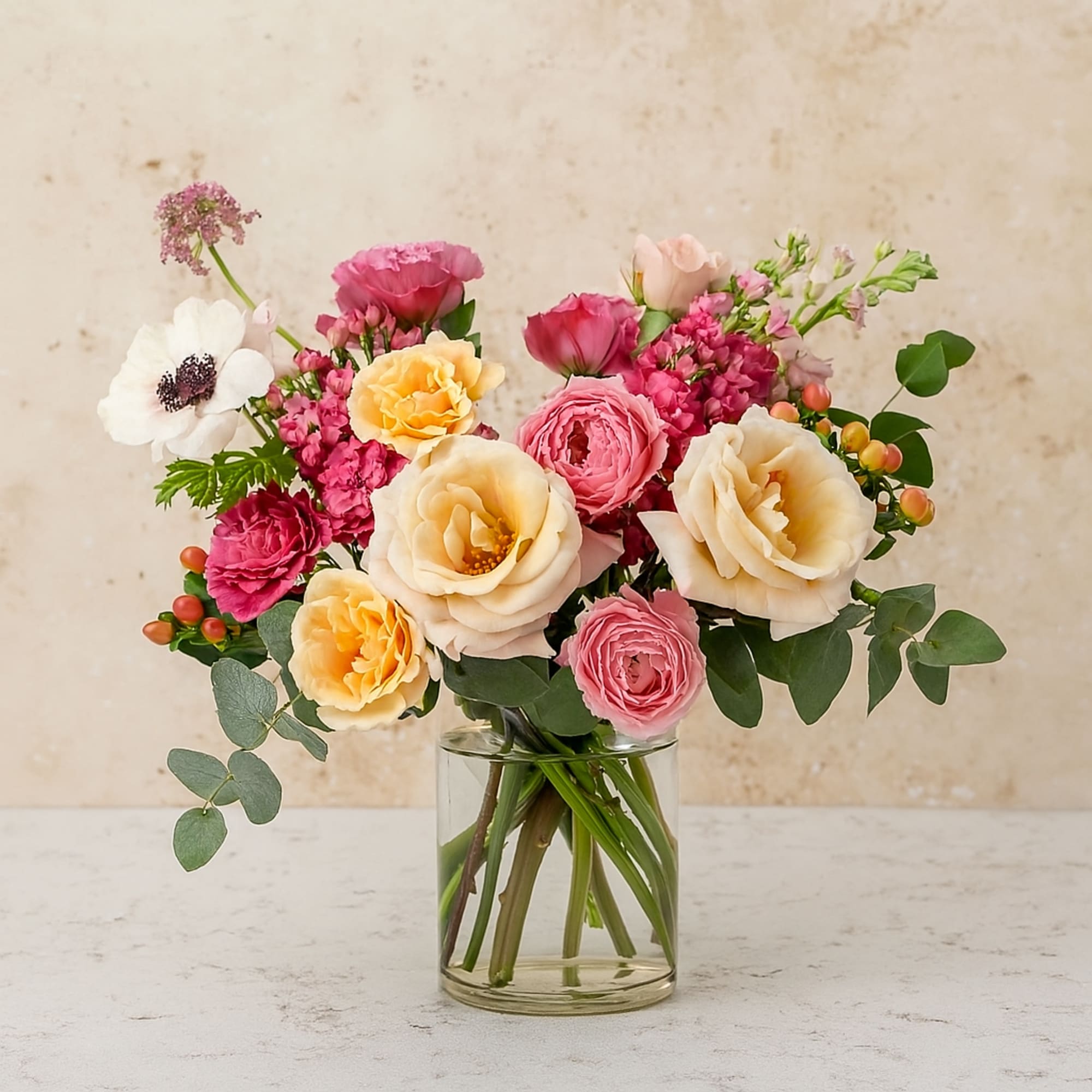 A graceful blend of blush-pink and peach garden roses, vibrant ranunculus, a