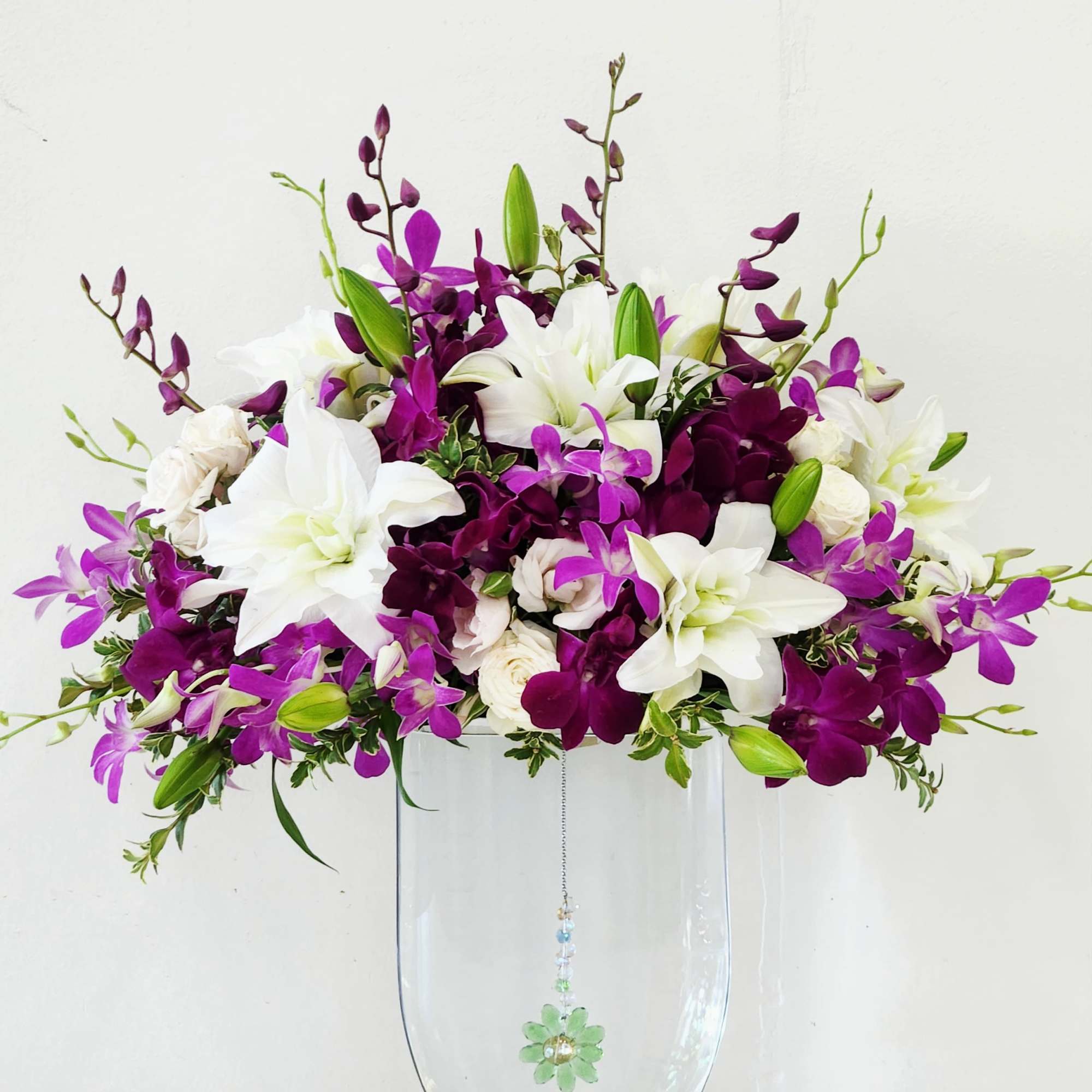 Purple orchids and delicate white rose lilies dance around a stunning tall