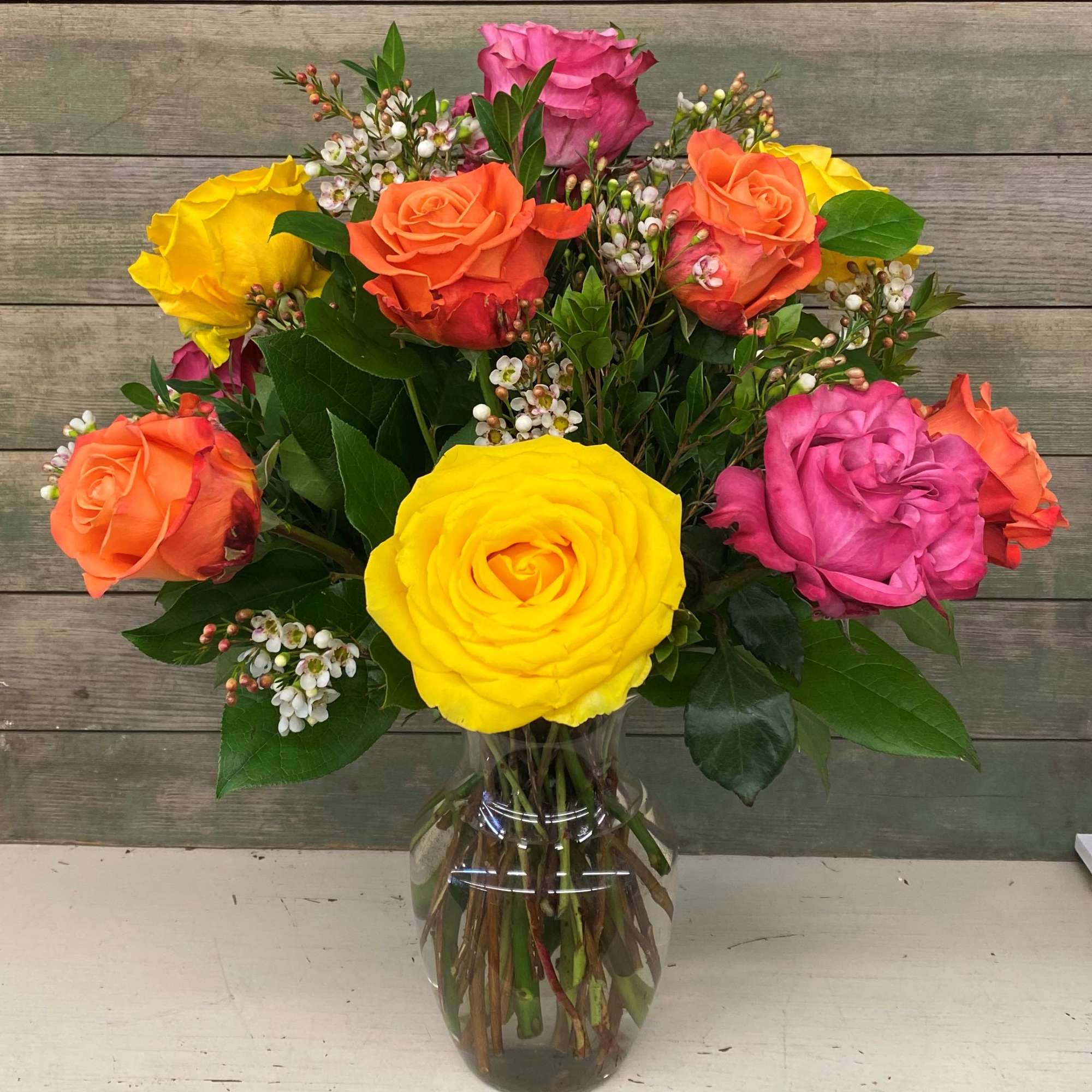 This classic arrangement features 12 mixed colored roses with premium greens and