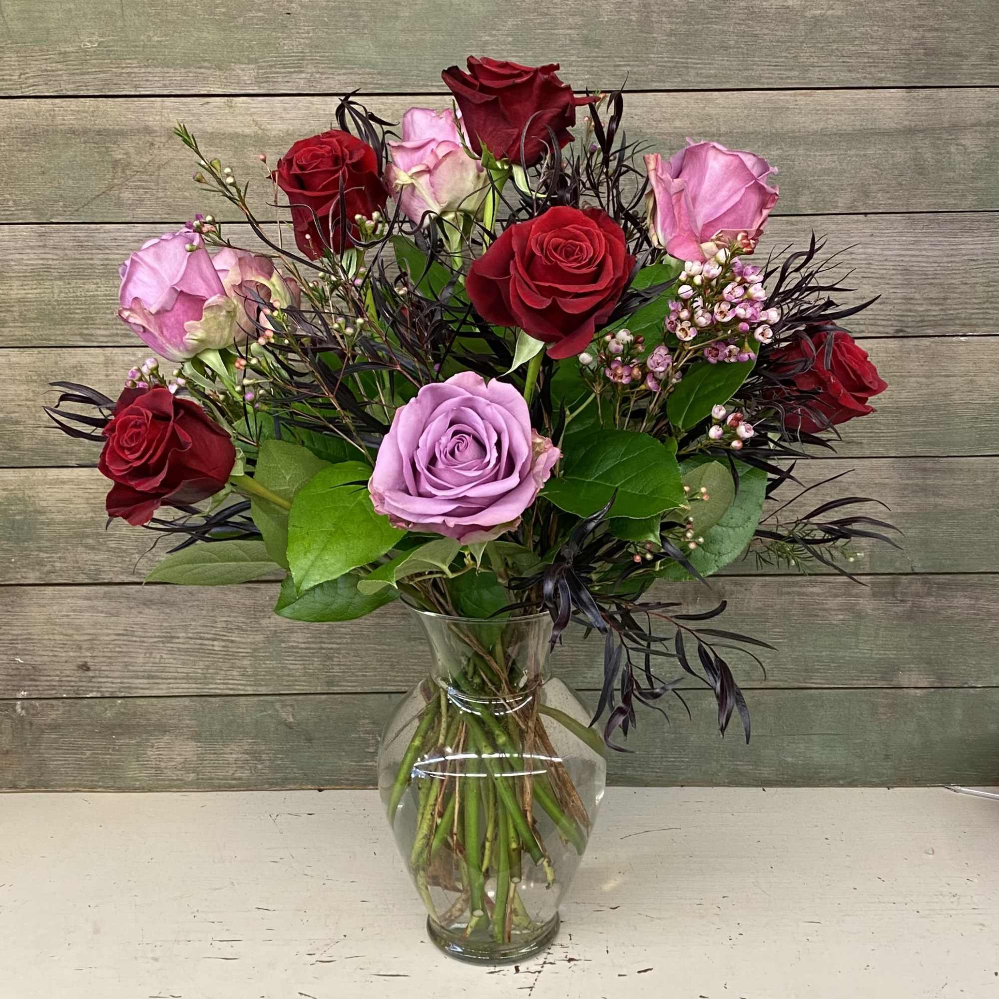 This classic arrangement features 12 mixed colored roses with premium greens and