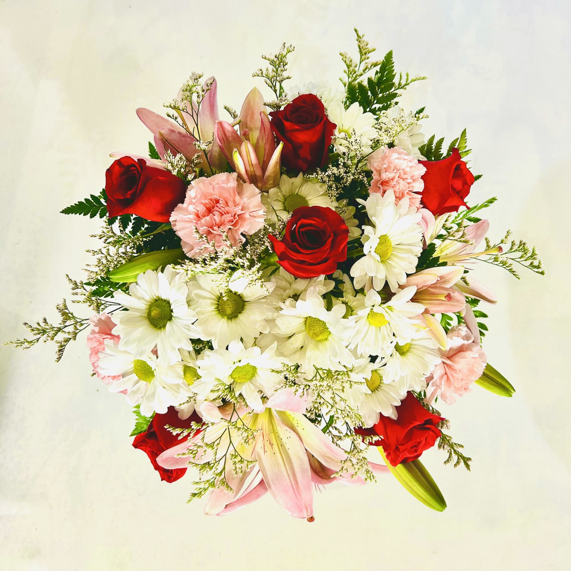 Featuring a combination of pink lilies, red roses, pink carnations, white daisies