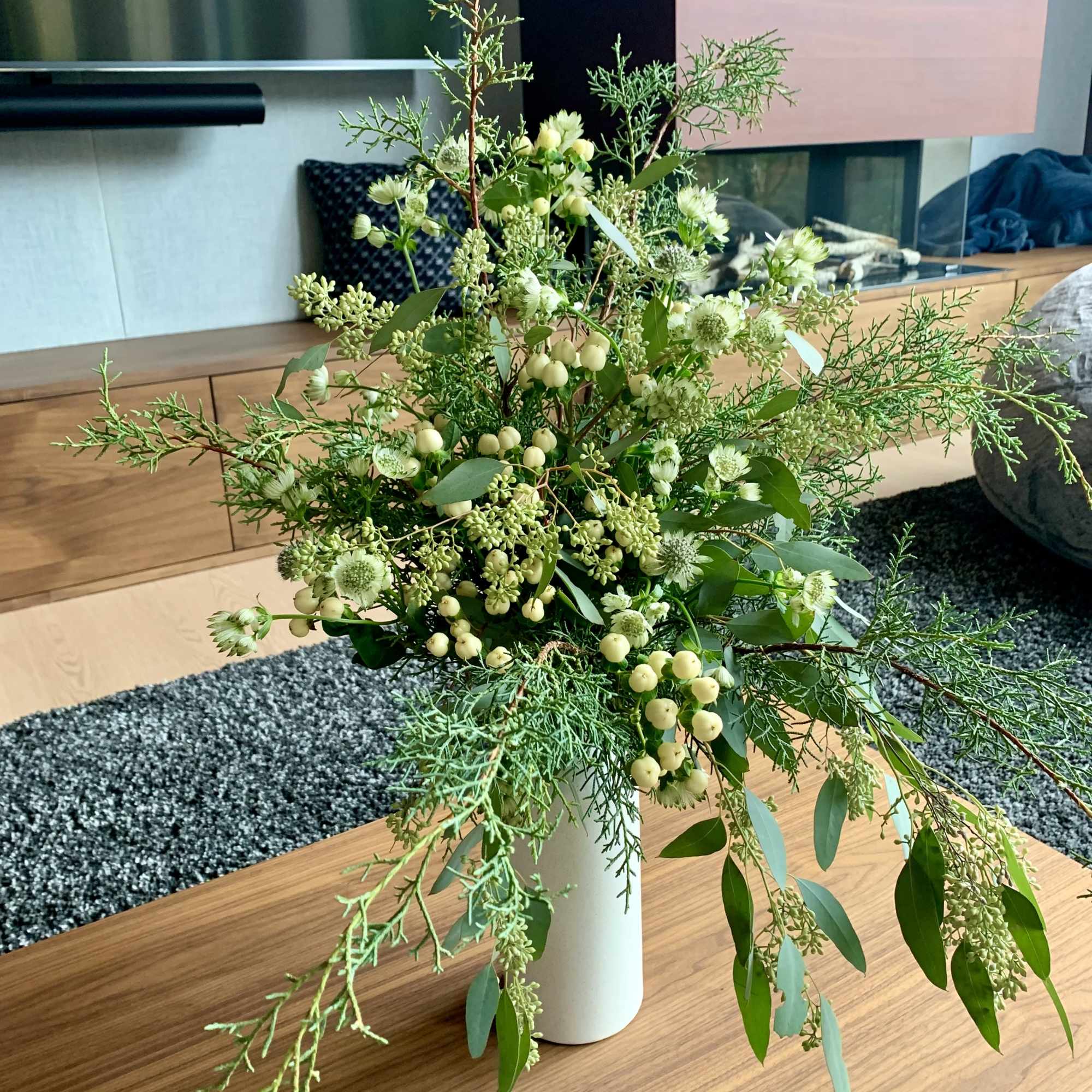 A tall fragrant holiday flower arrangement with lots of wintergreens, eucalyptus, white