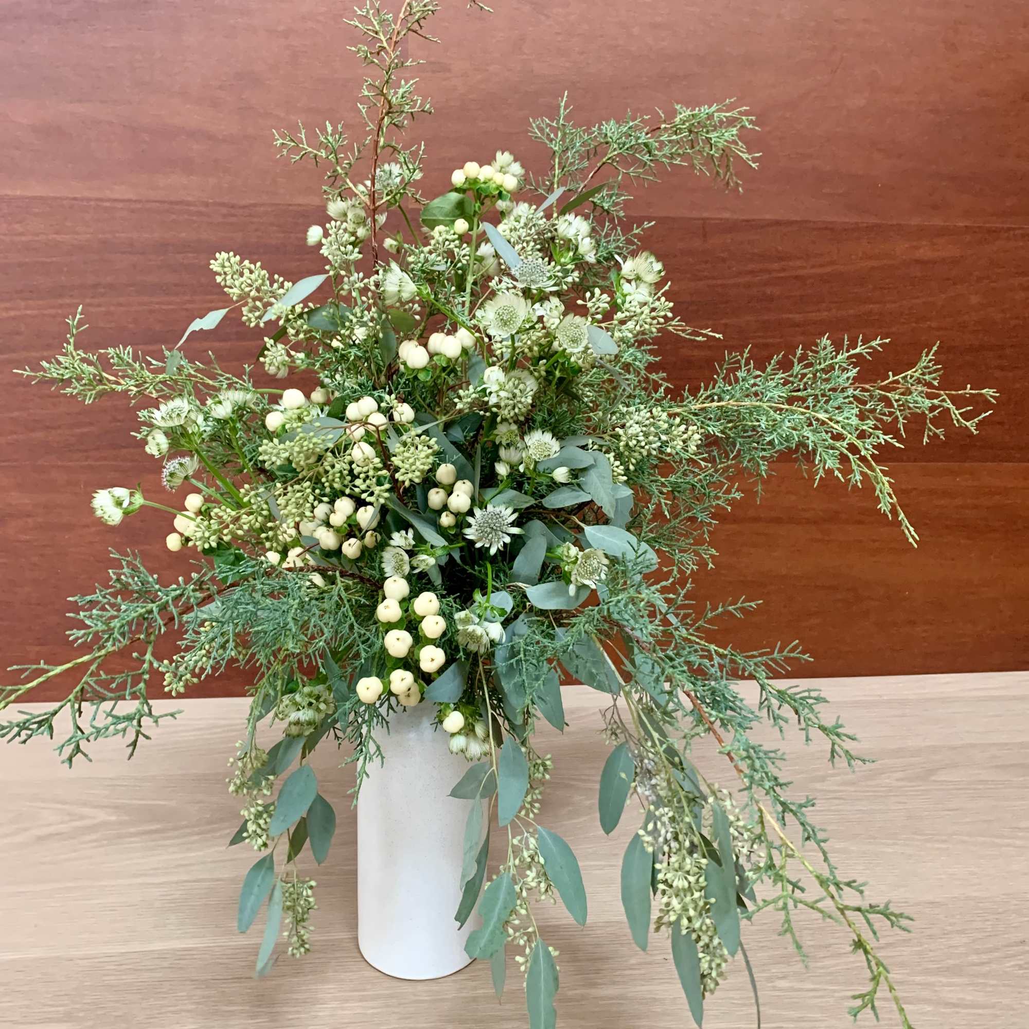 A tall fragrant holiday flower arrangement with lots of wintergreens, eucalyptus, white