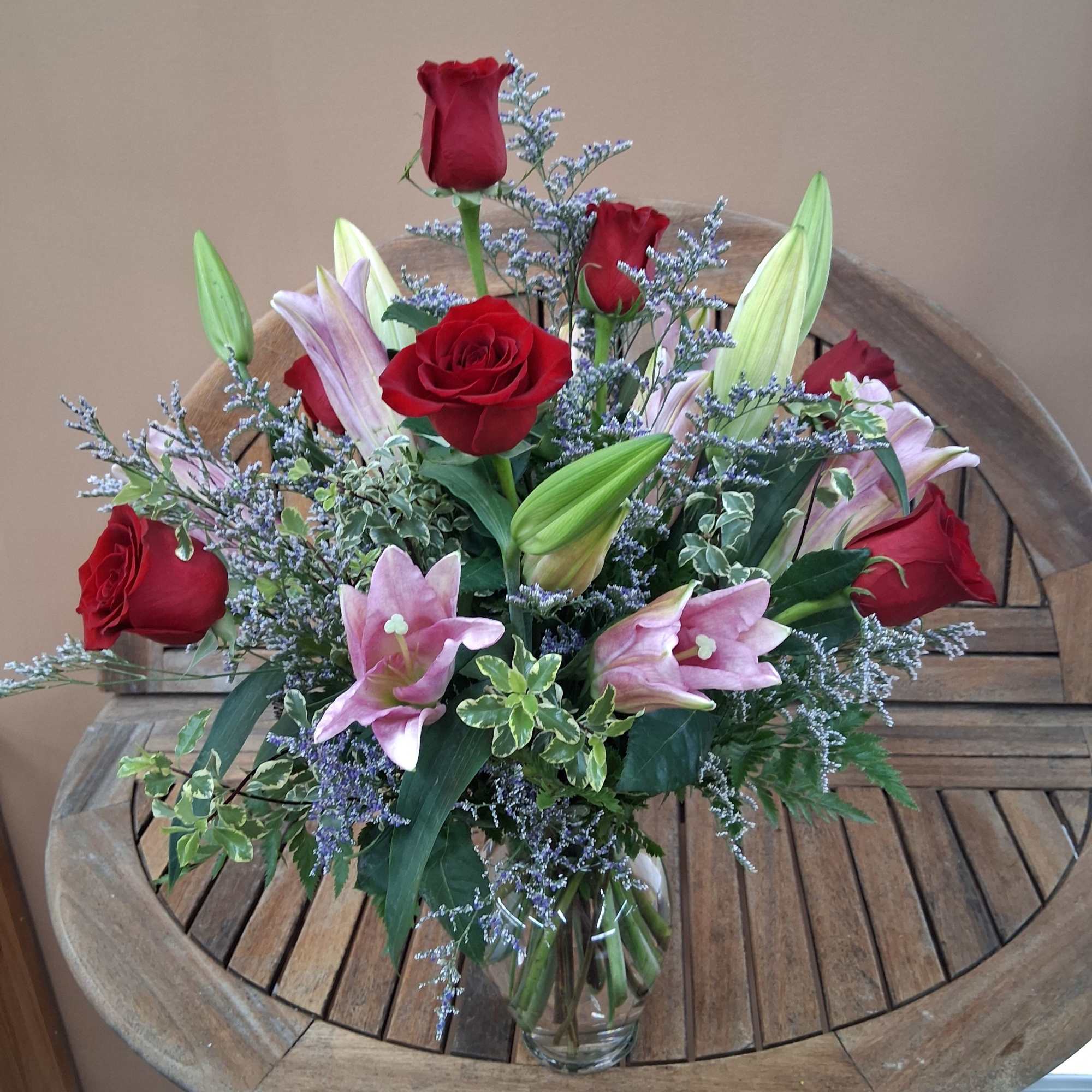 Red roses and pink lilies arranged in a vase with greens and