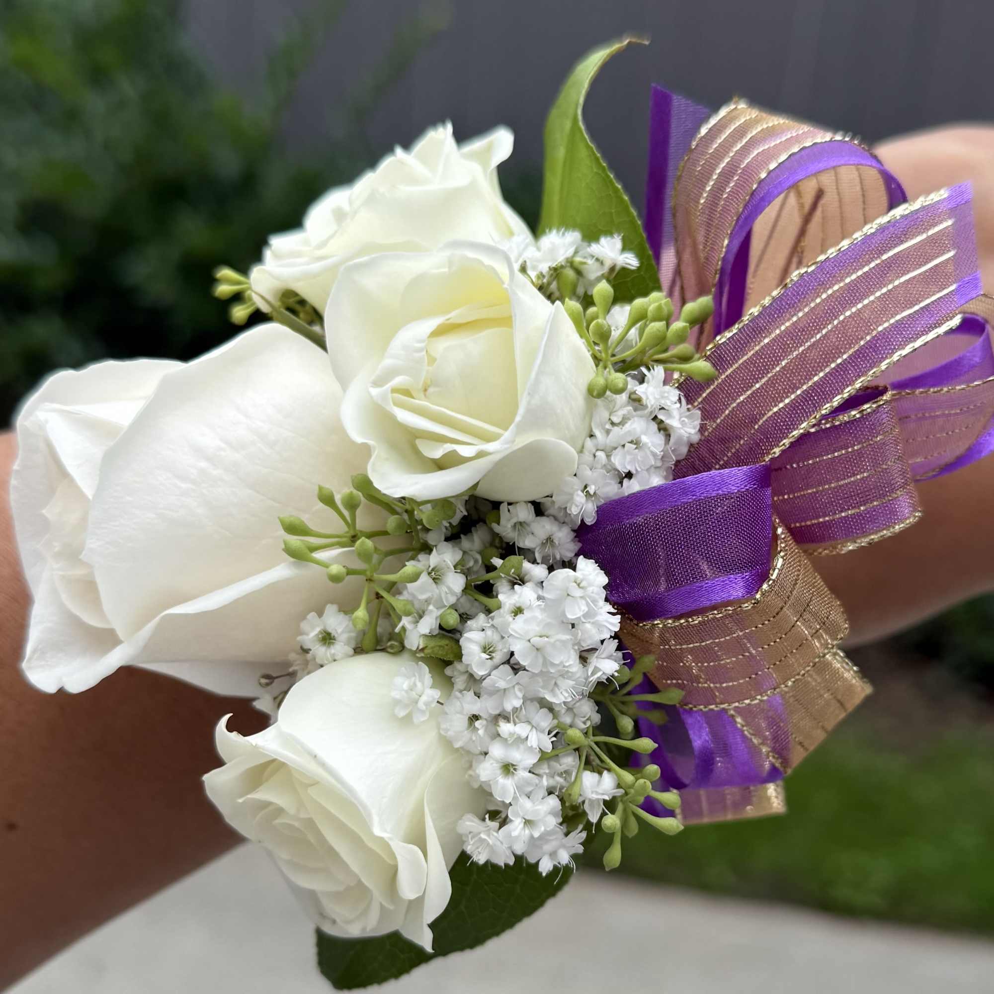 Beautiful corsage bracelet designed with white spray roses, seasonal greenery, and white