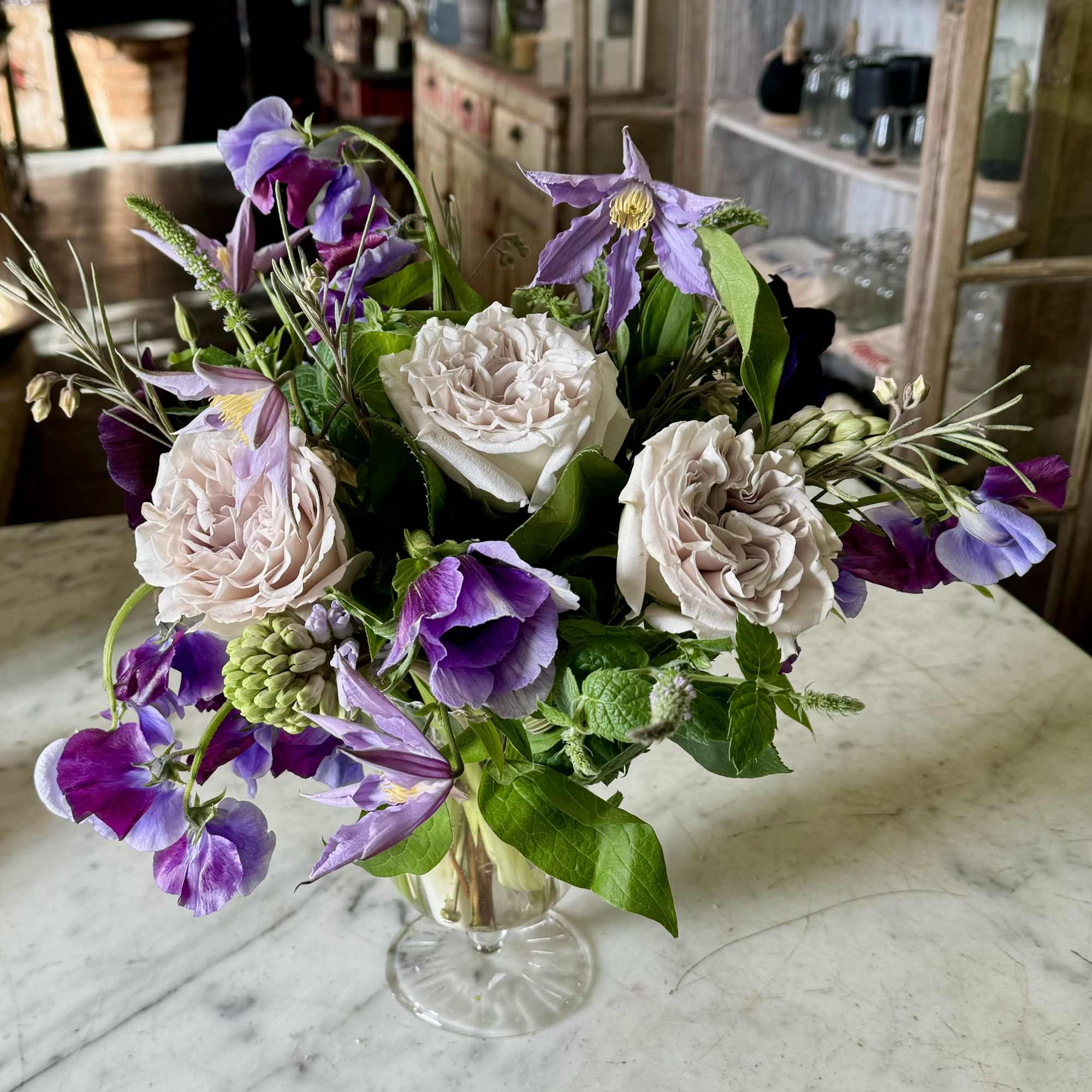 A footed delicate glass vase filled with seasonal blooms in lavenders to
