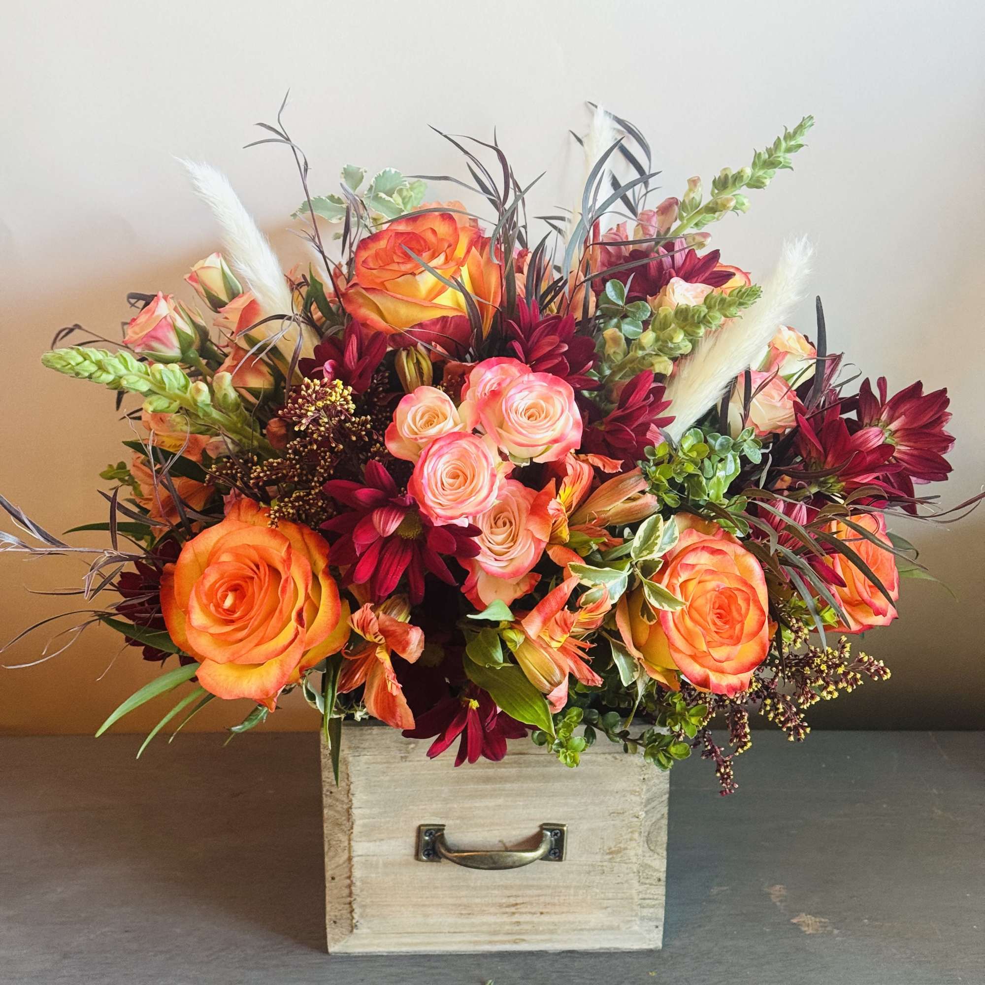 A vibrant arrangement with bight orange roses, burgundy cymbidium roses, and green