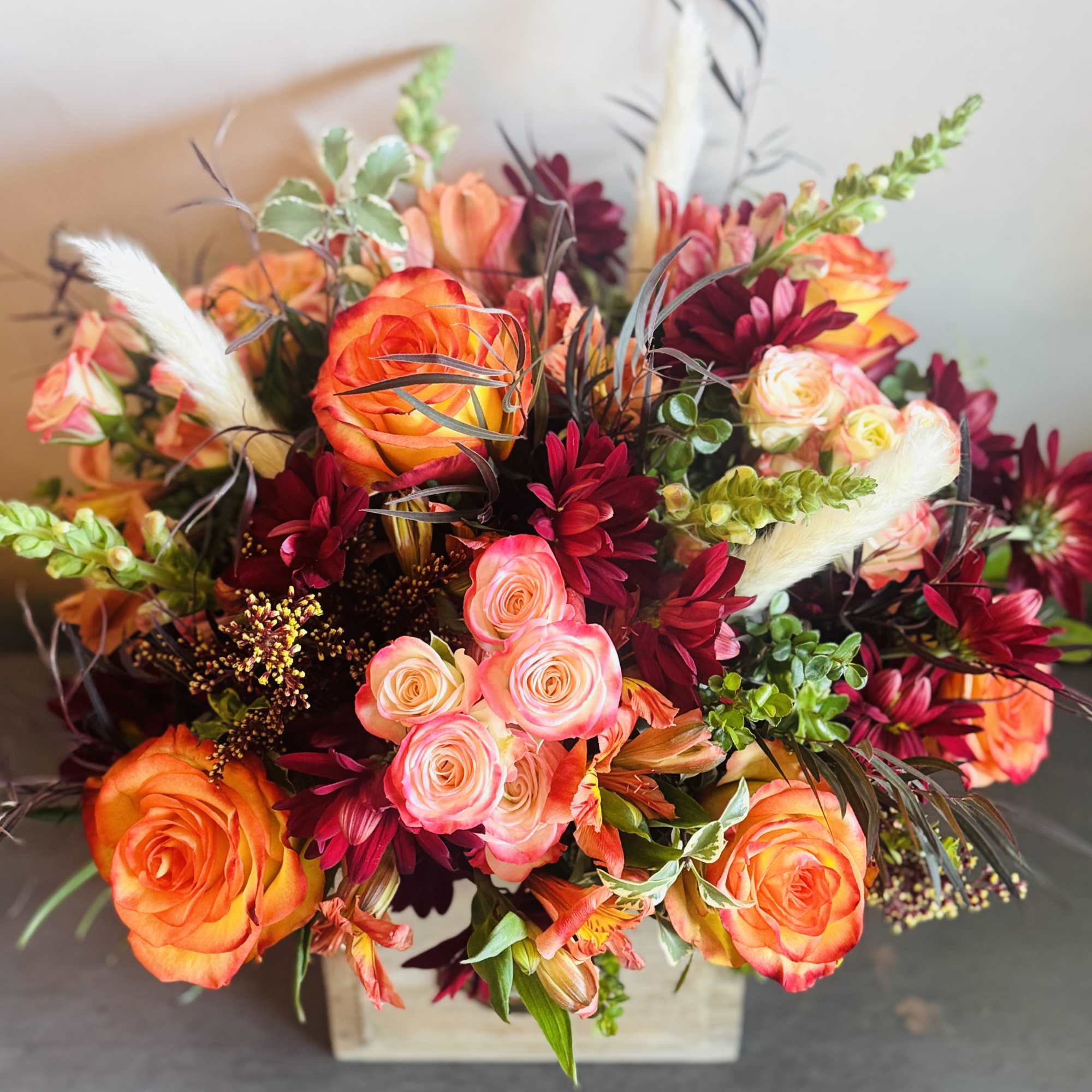 A vibrant arrangement with bight orange roses, burgundy cymbidium roses, and green