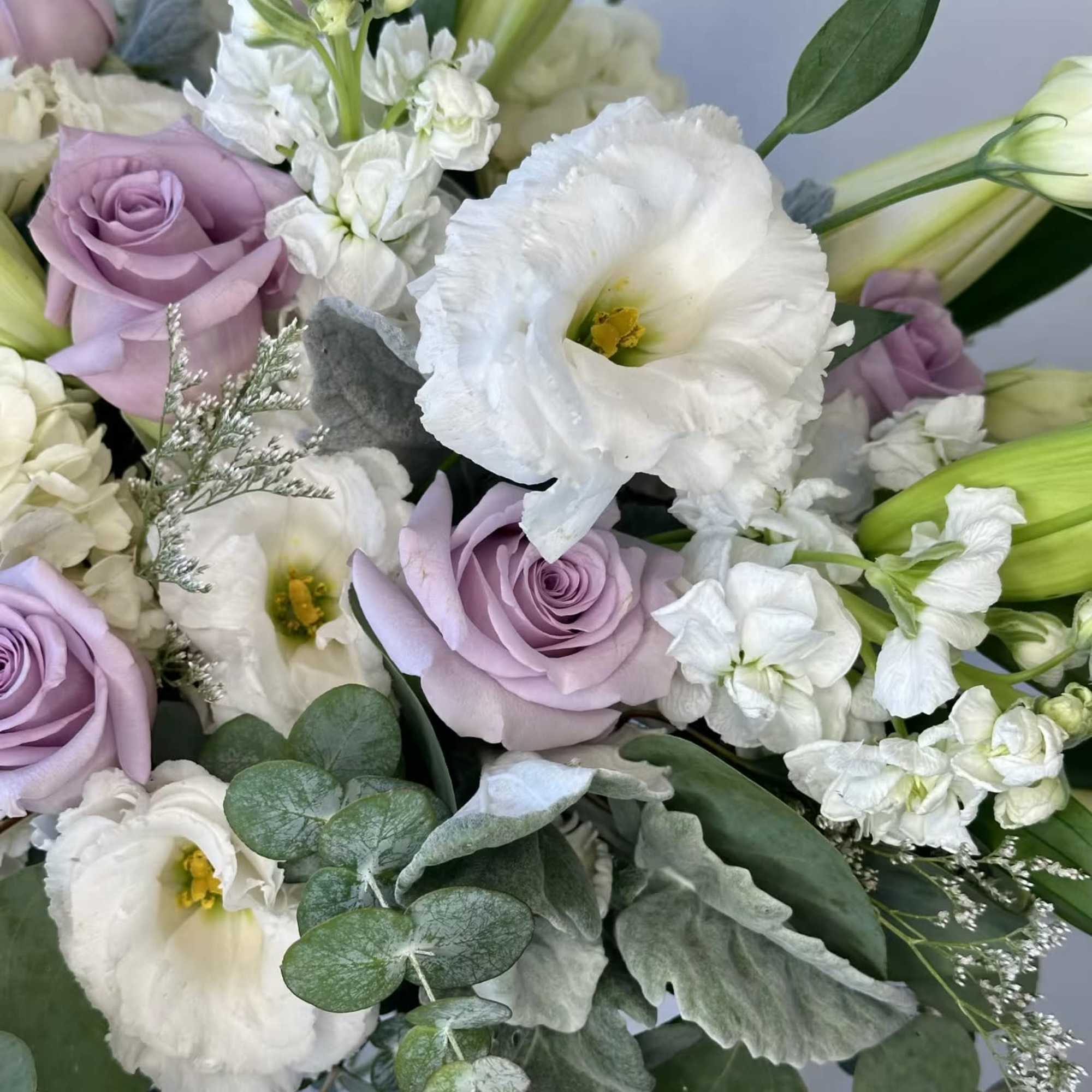 This bouquet consists of white lilies, white lisianthus, purple roses, white hydrangea