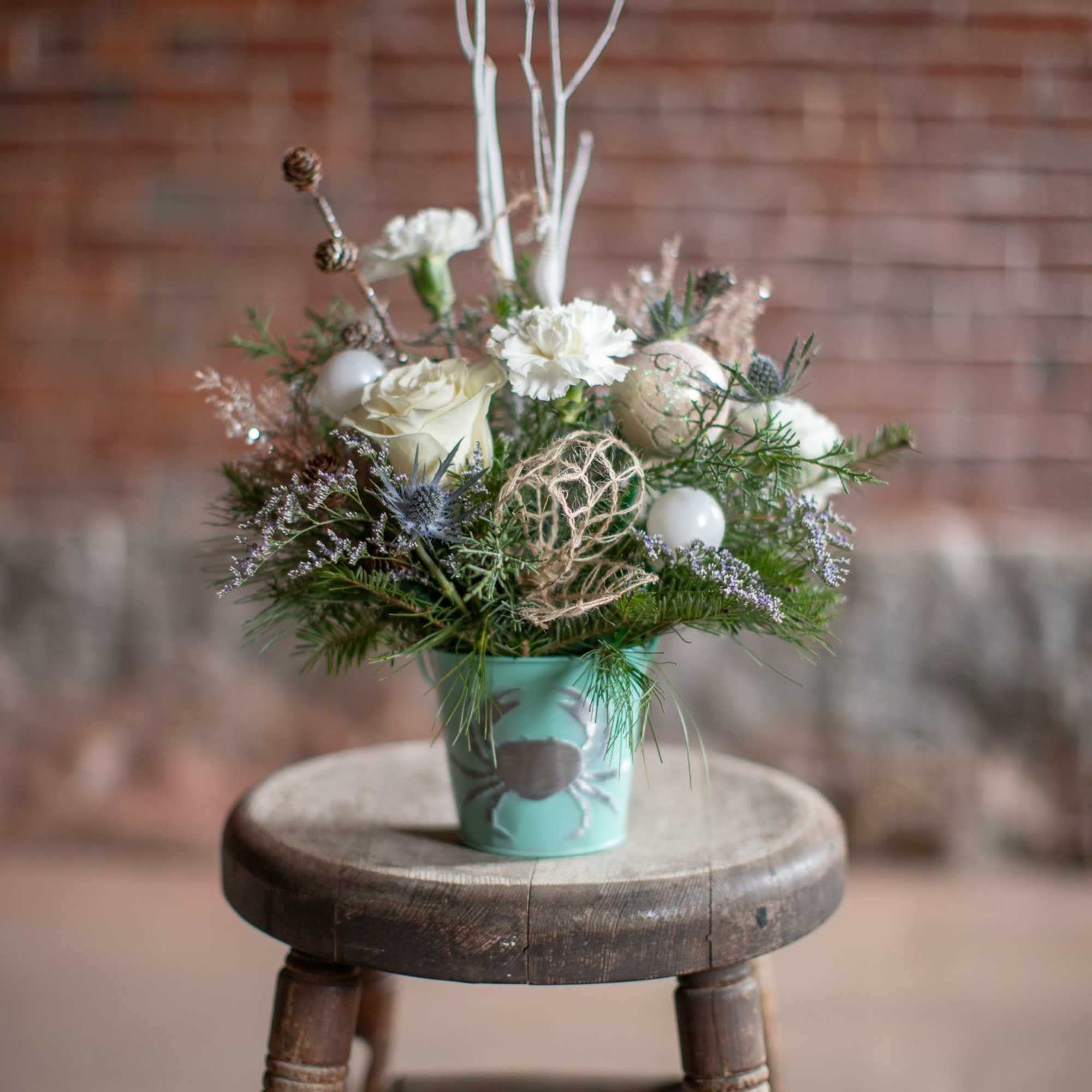 Winter foliage is artfully arranged in a coastal inspired tin container. This