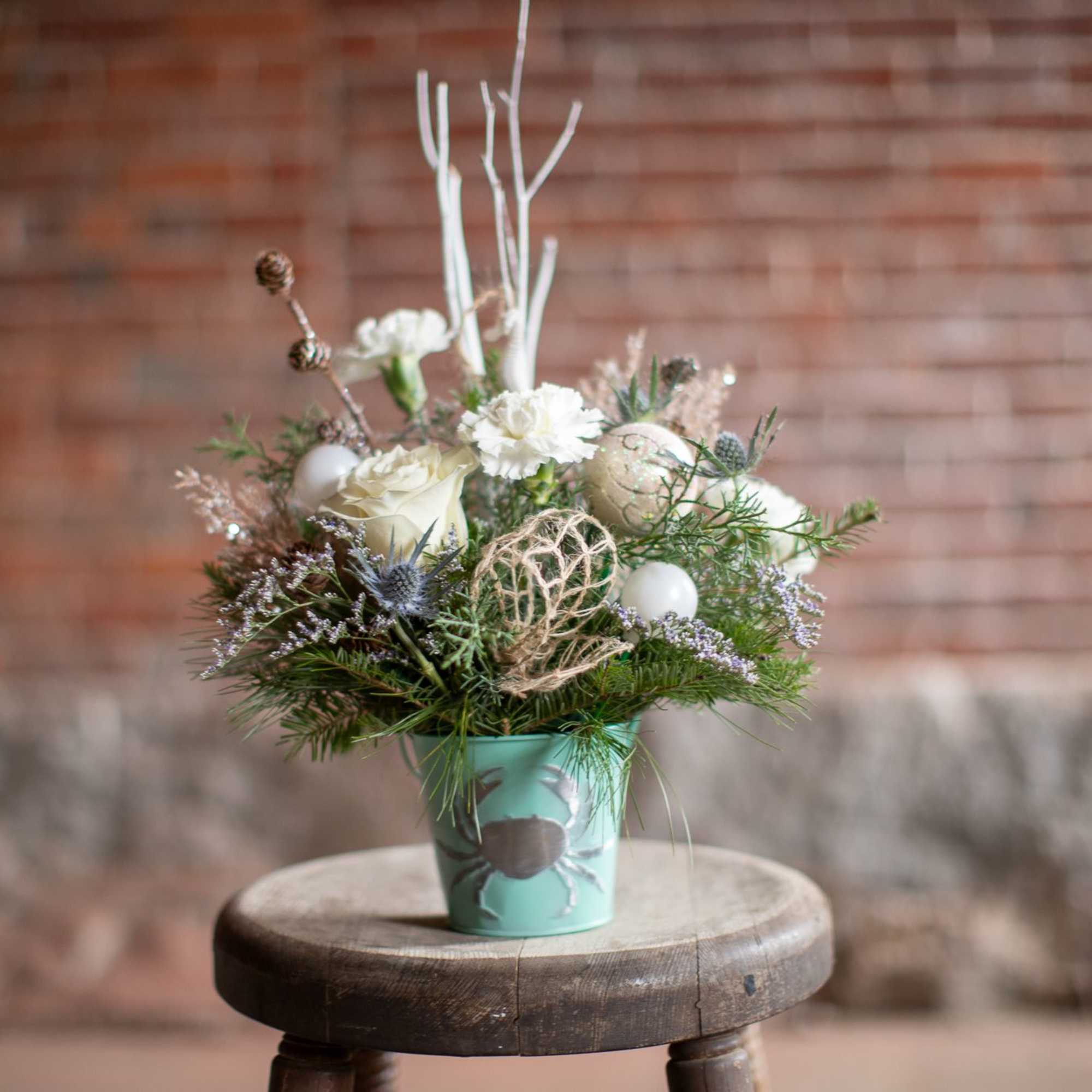 Winter foliage is artfully arranged in a coastal inspired tin container. This