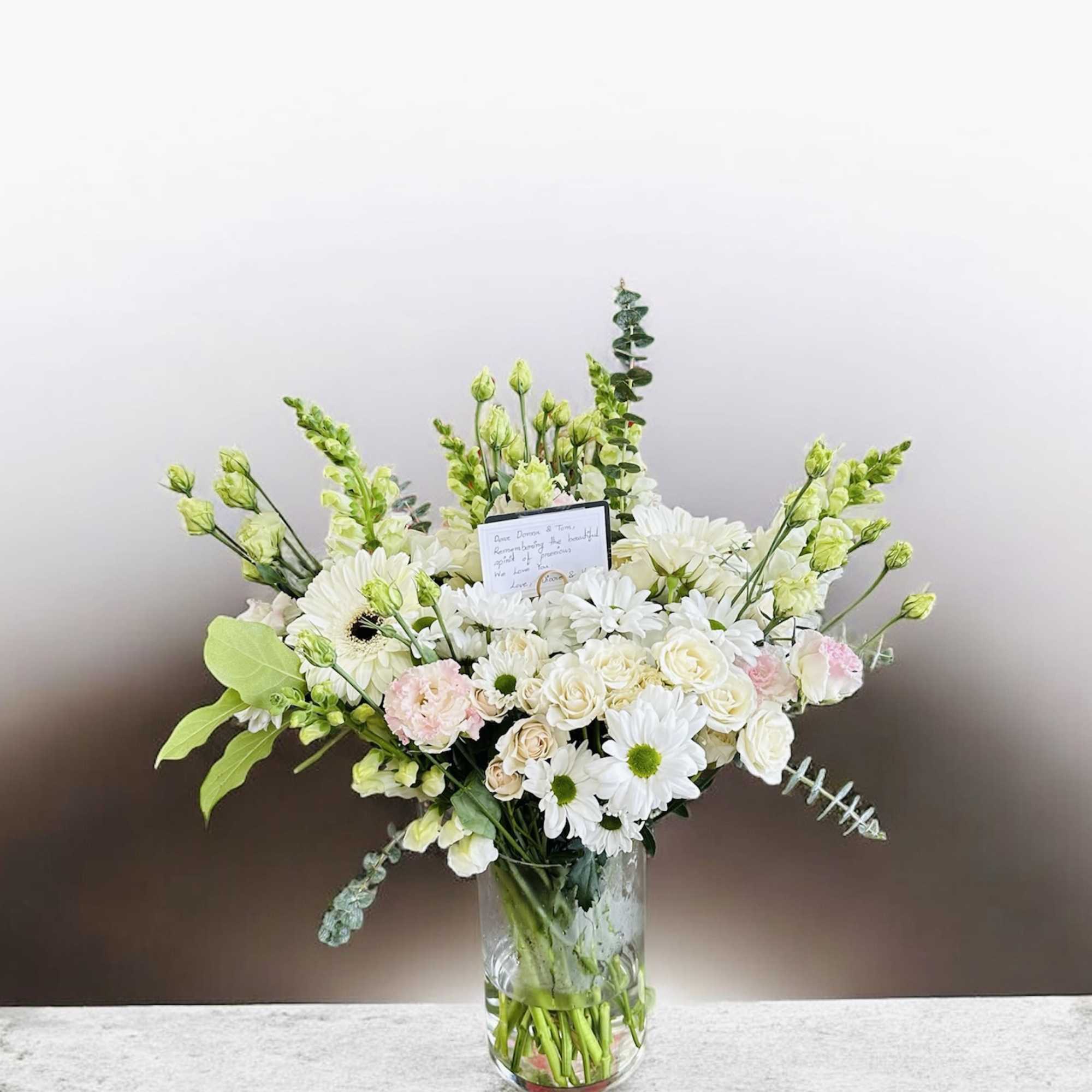 A soft, airy arrangement featuring cream roses, white daisies, and pink snapdragons