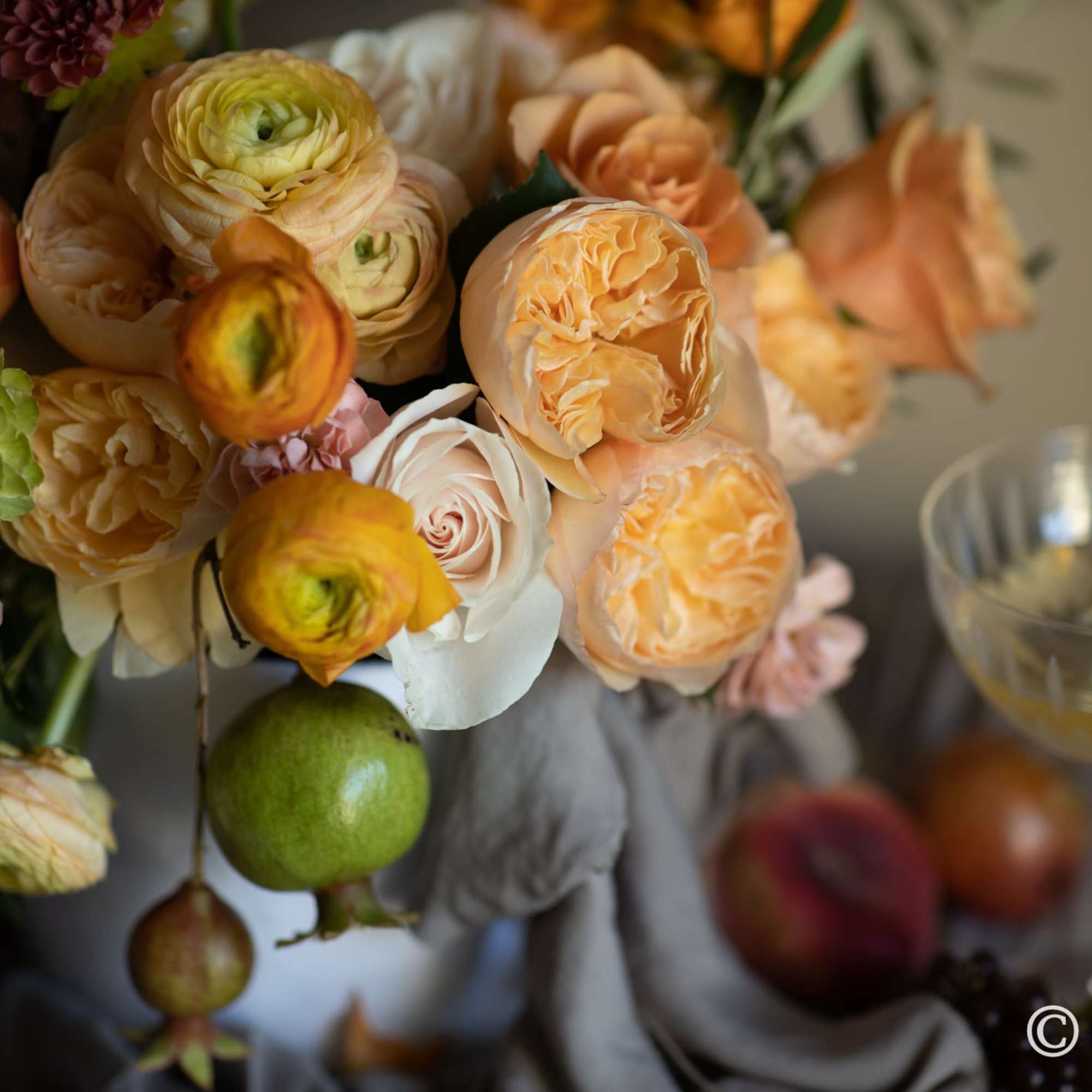 Floral arrangement in warm hues (orange, yellow, peach, burgundy, etc.) presented in