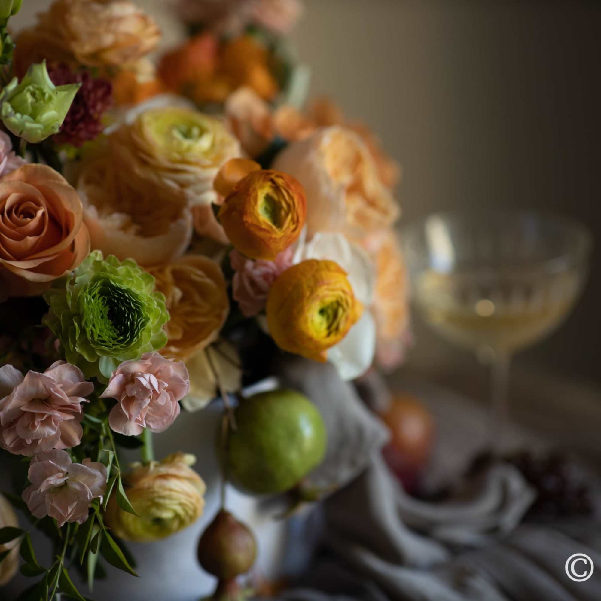 Floral arrangement in warm hues (orange, yellow, peach, burgundy, etc.) presented in