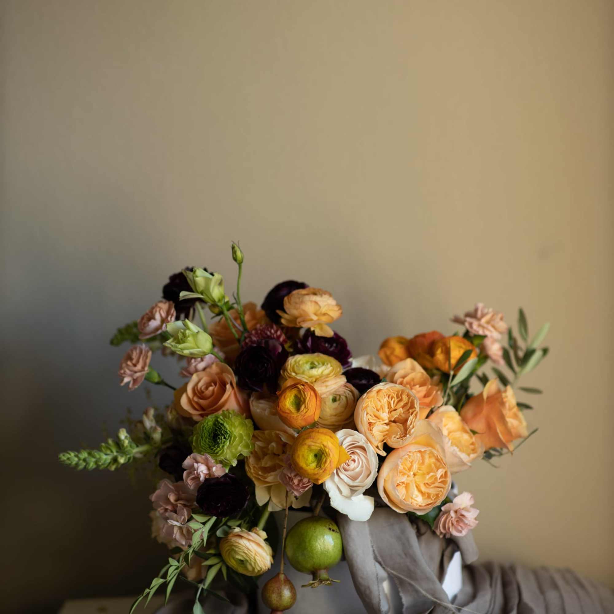 Floral arrangement in warm hues (orange, yellow, peach, burgundy, etc.) presented in