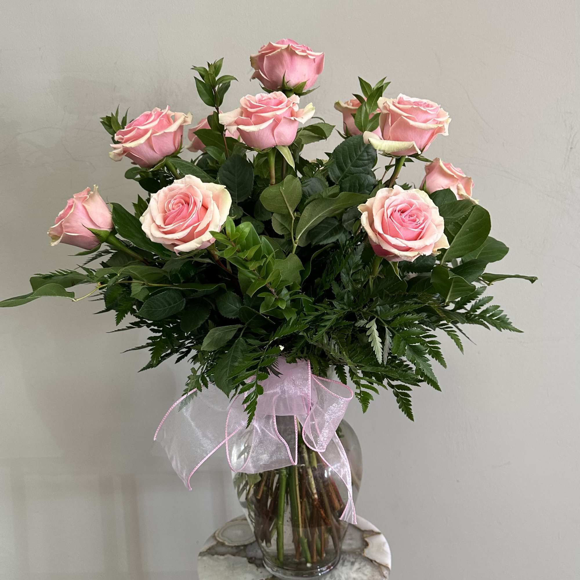 A dozen long stem medium pink roses with assorted greenery in a