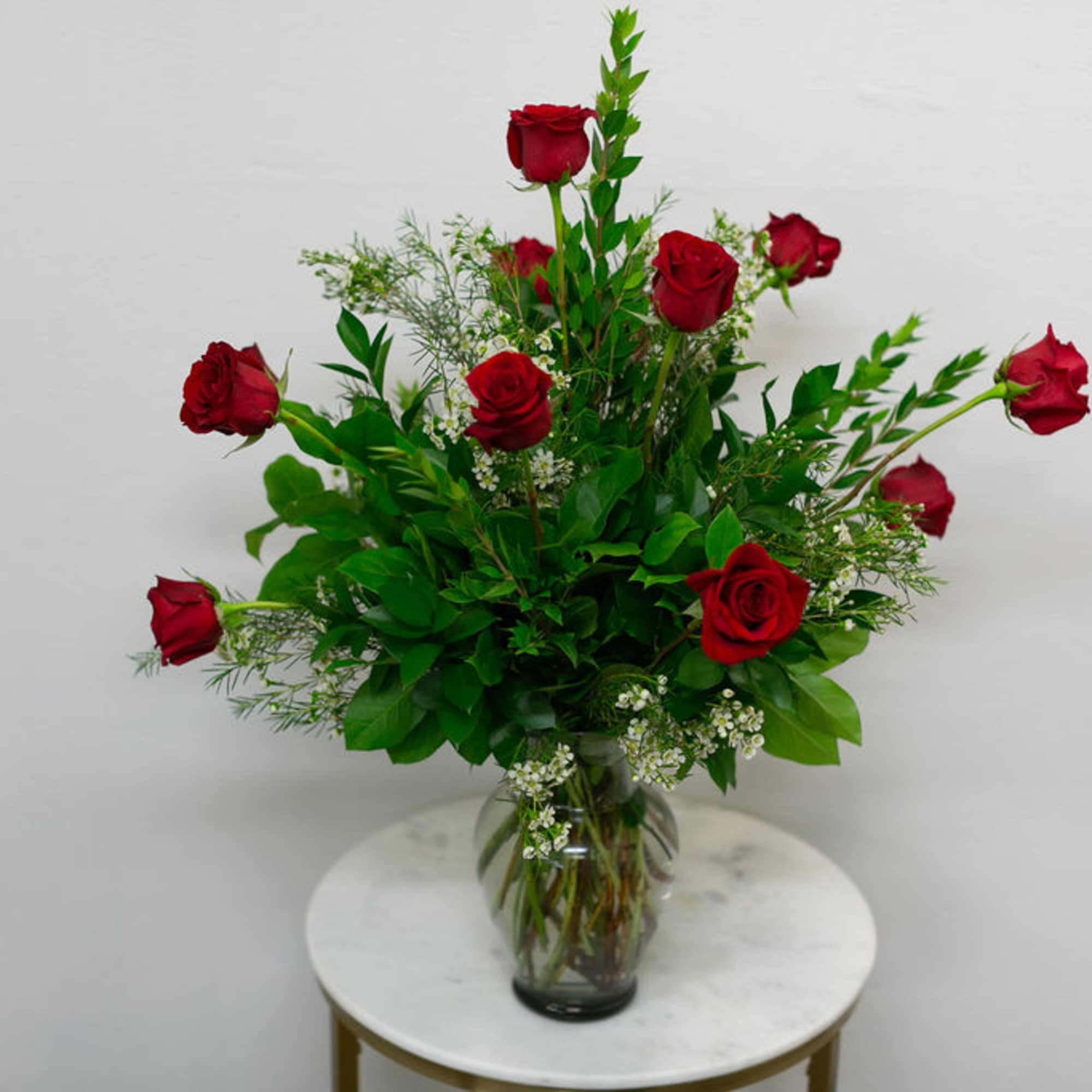 12 Red Roses arranged with greenery and filler in a simple vase.