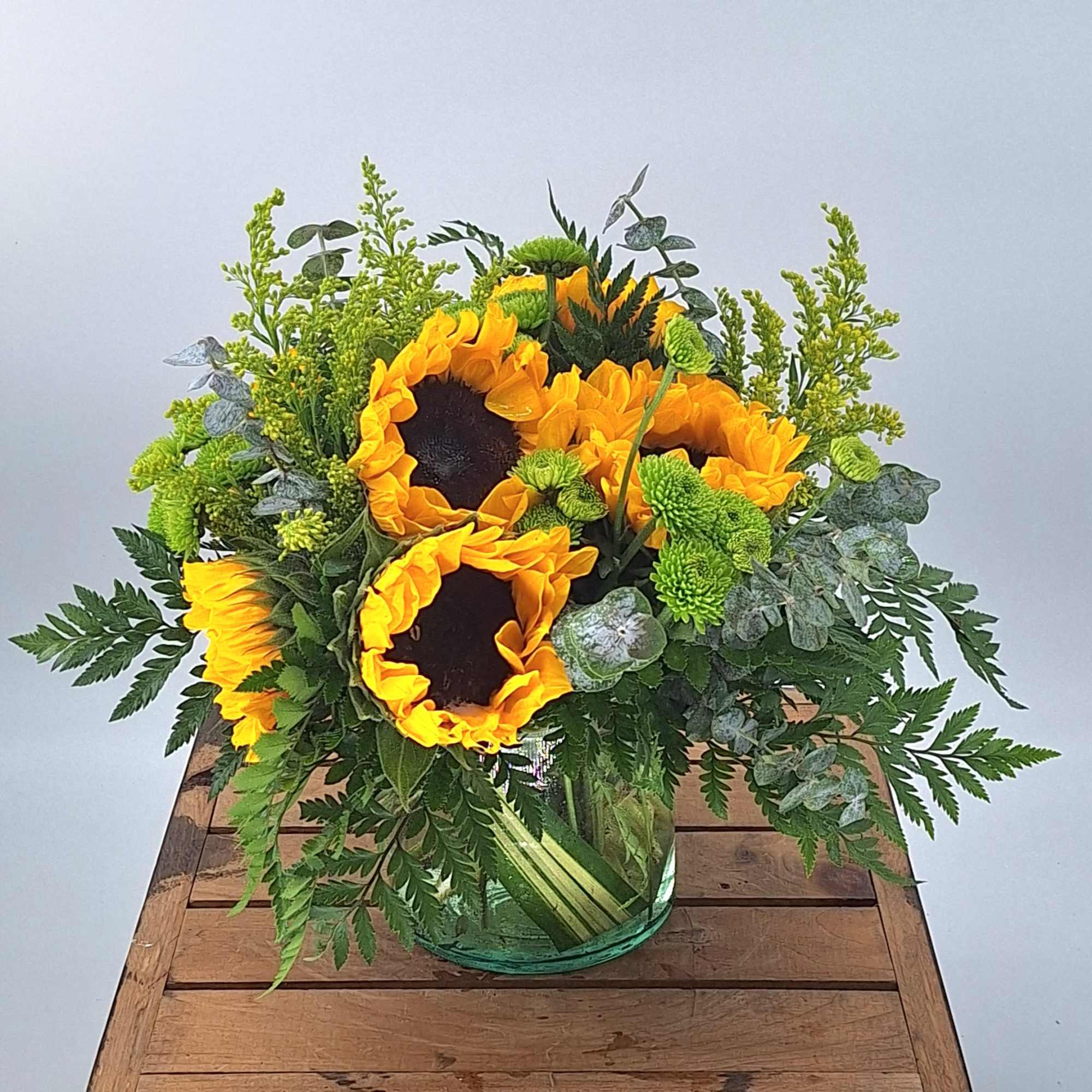 Introducing our cheerful and vibrant flower arrangement featuring sunflowers in a leaf-lined