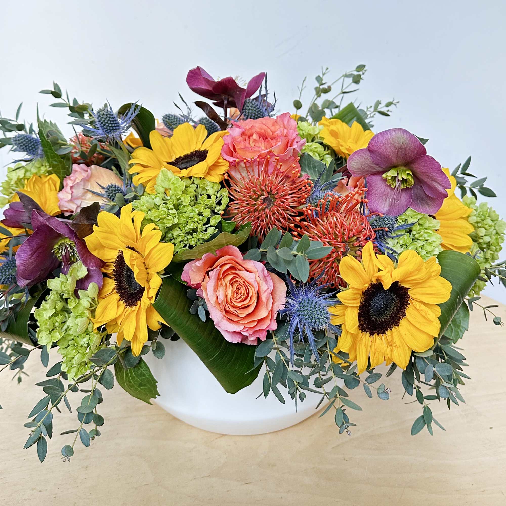 This arrangement includes sunflowers, green hydrangeas, pincushions, free spirit roses, burgundy hellebore