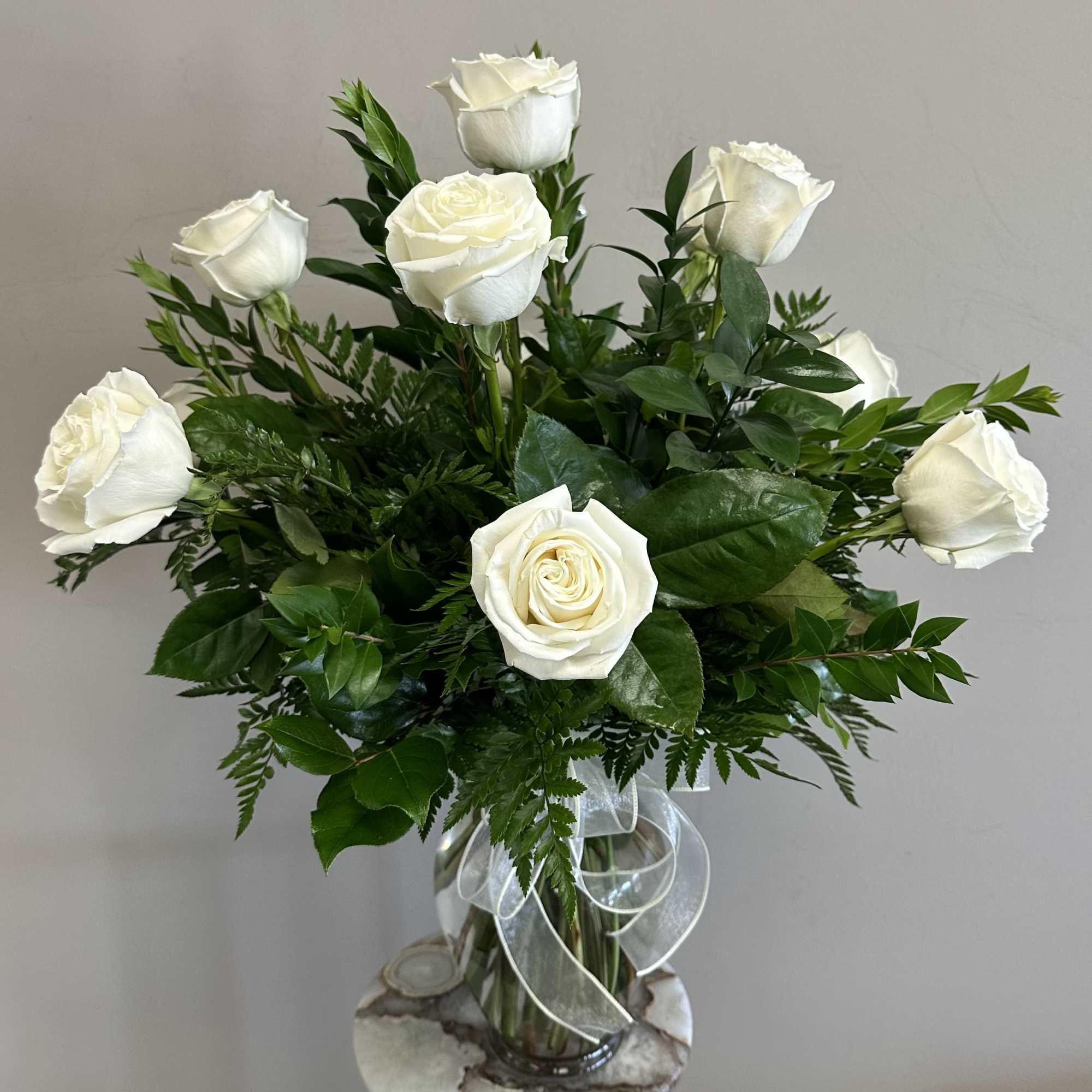 A dozen long stem white roses with assorted greenery in a clear