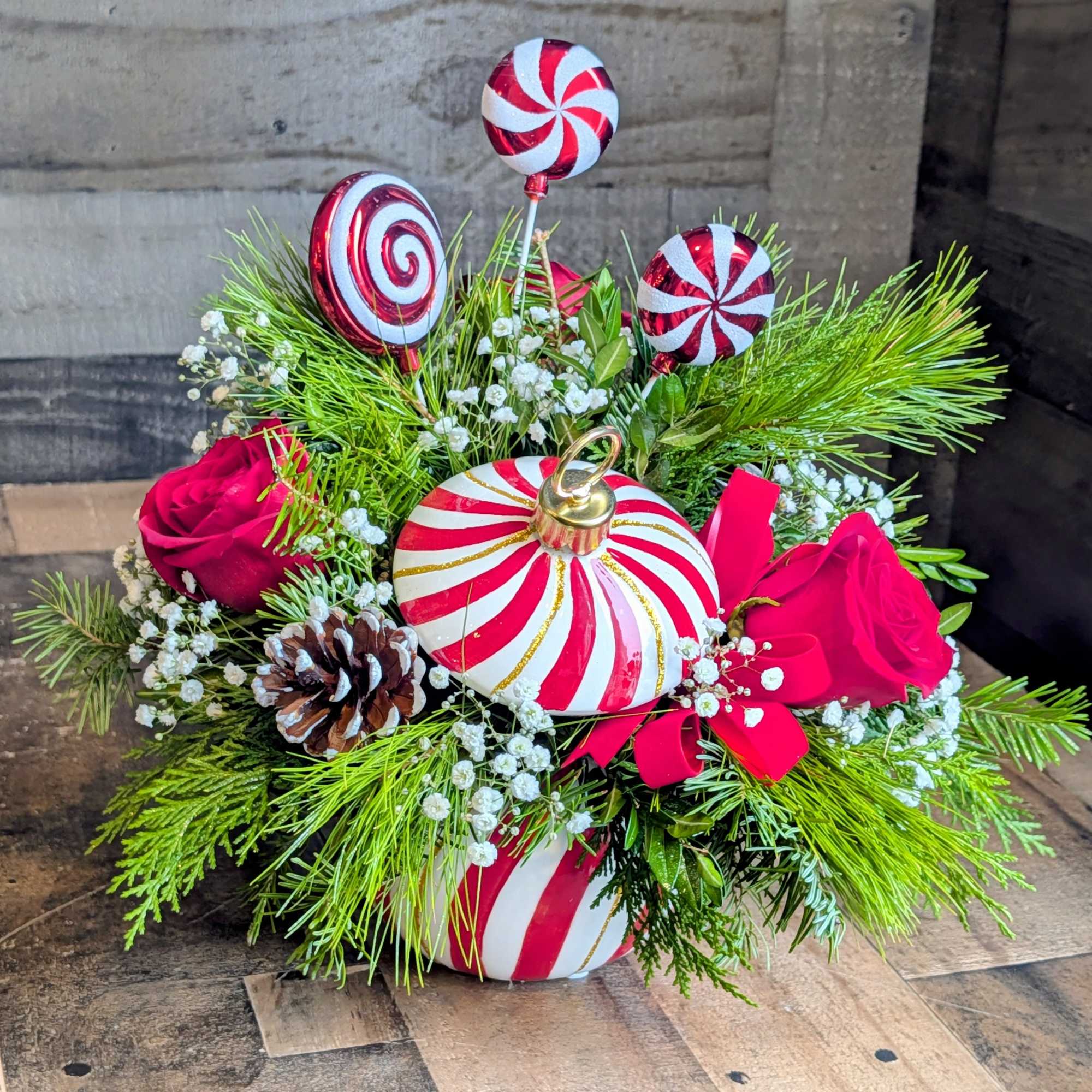 Shown as Standard
Red roses, babies breath, sparkly evergreens, and pinecones comes arranged