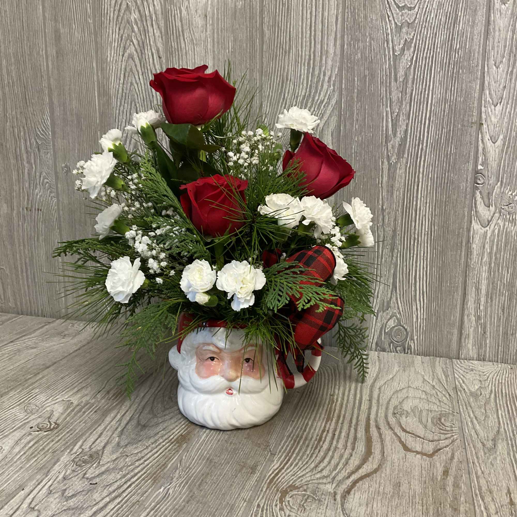 A cozy Christmas arrangement of roses, carnations, pine and greenery in a