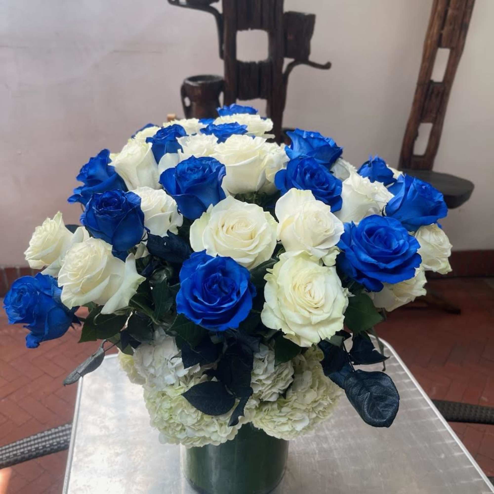 Nestled within a tall glass vase, delicate blue, and white roses intertwine