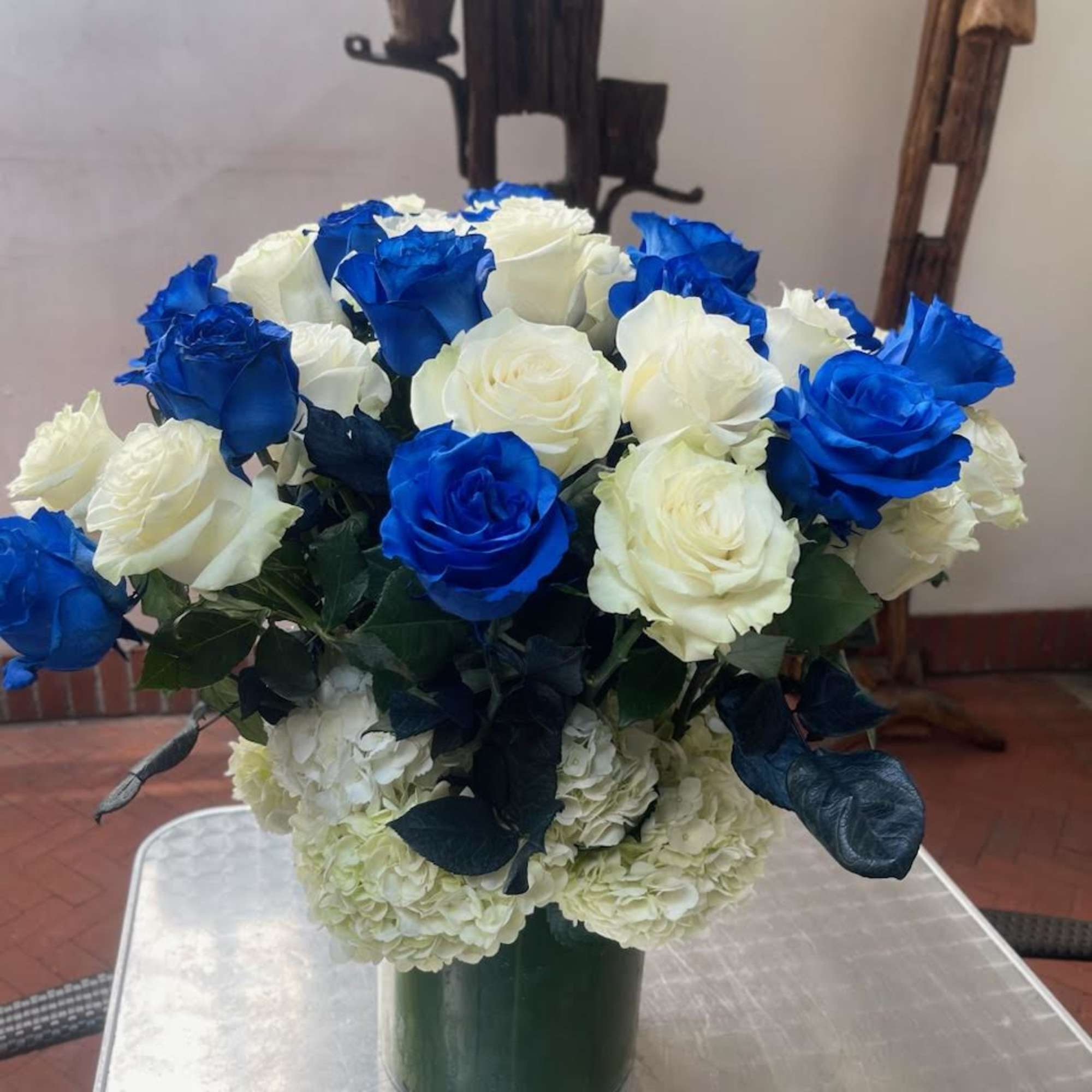 Nestled within a tall glass vase, delicate blue, and white roses intertwine