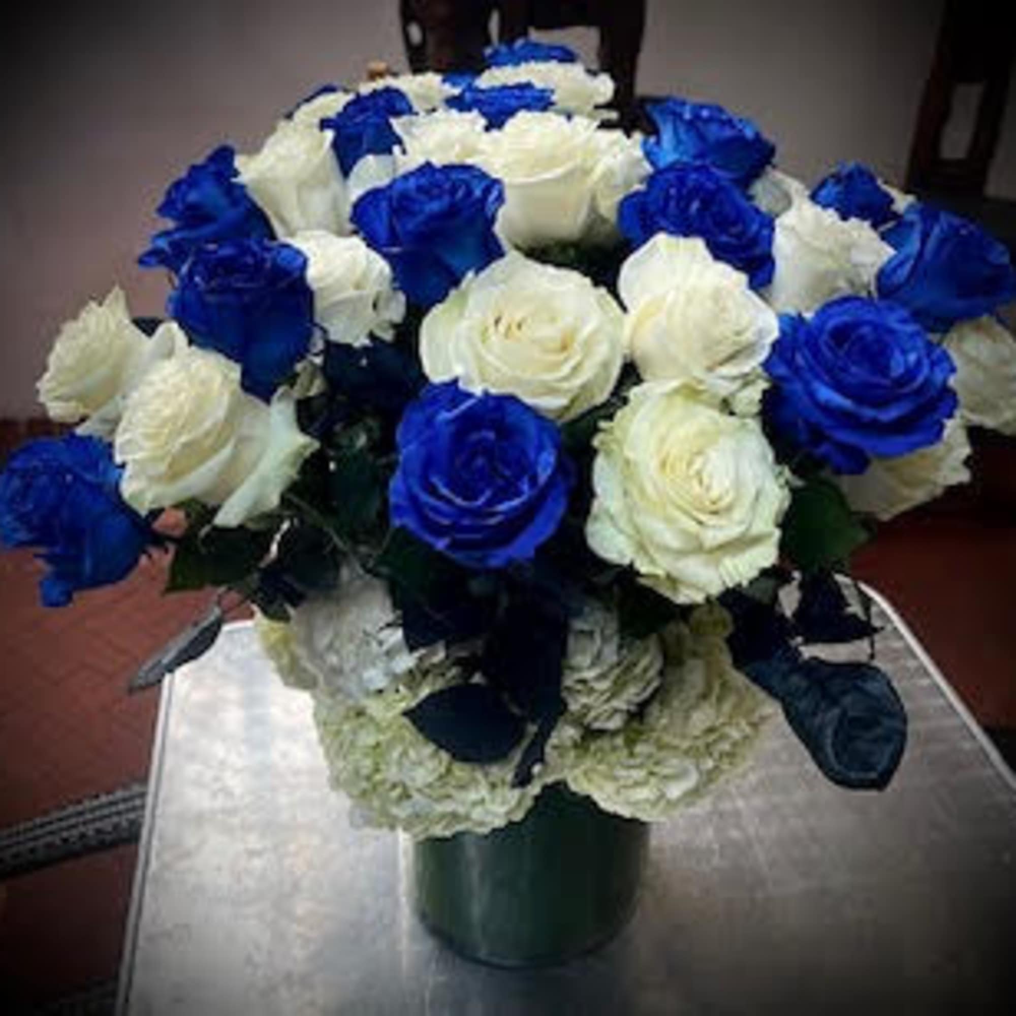 Nestled within a tall glass vase, delicate blue, and white roses intertwine