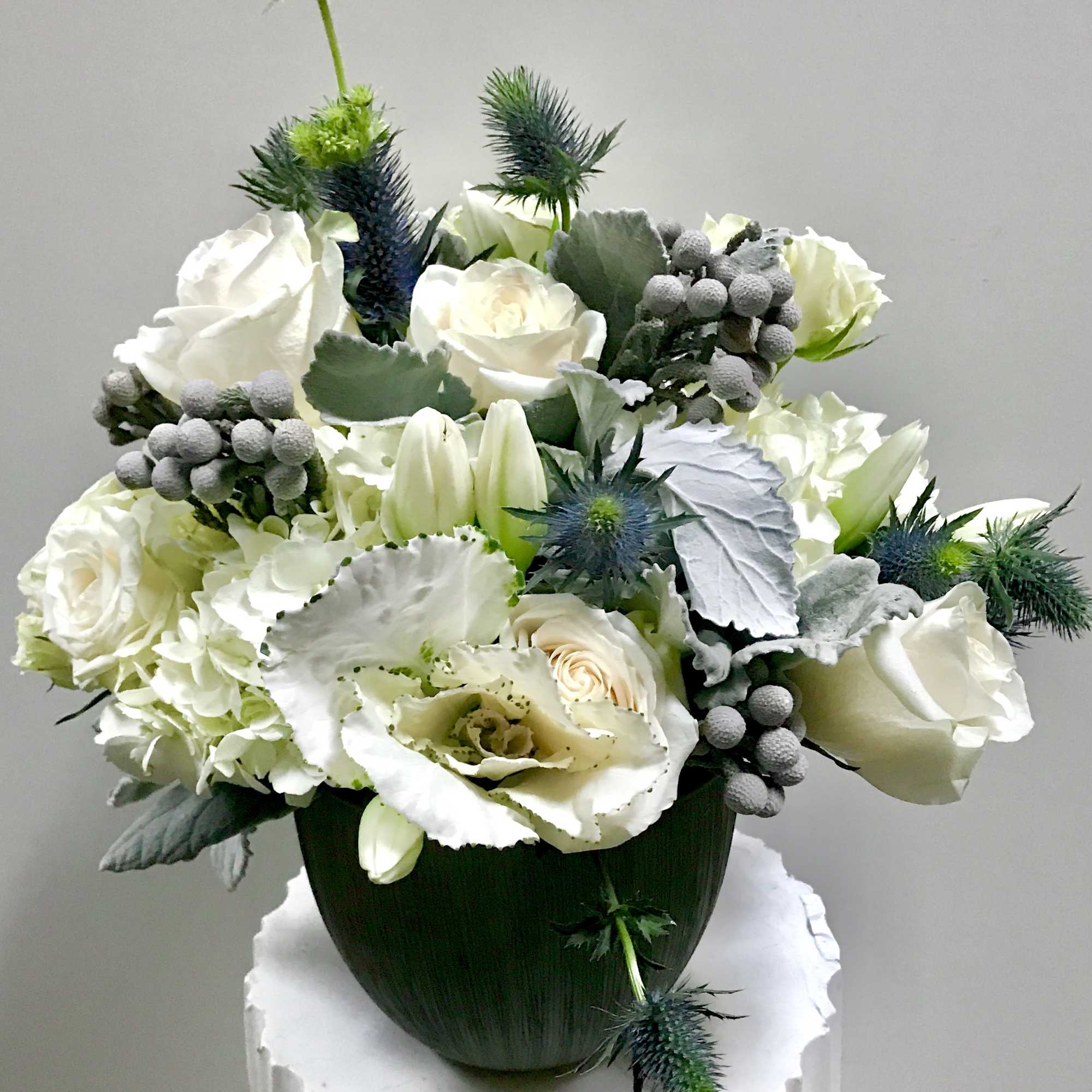 In a ceramic vase winter flowers of white roses,white tulips,white hydrangeas and