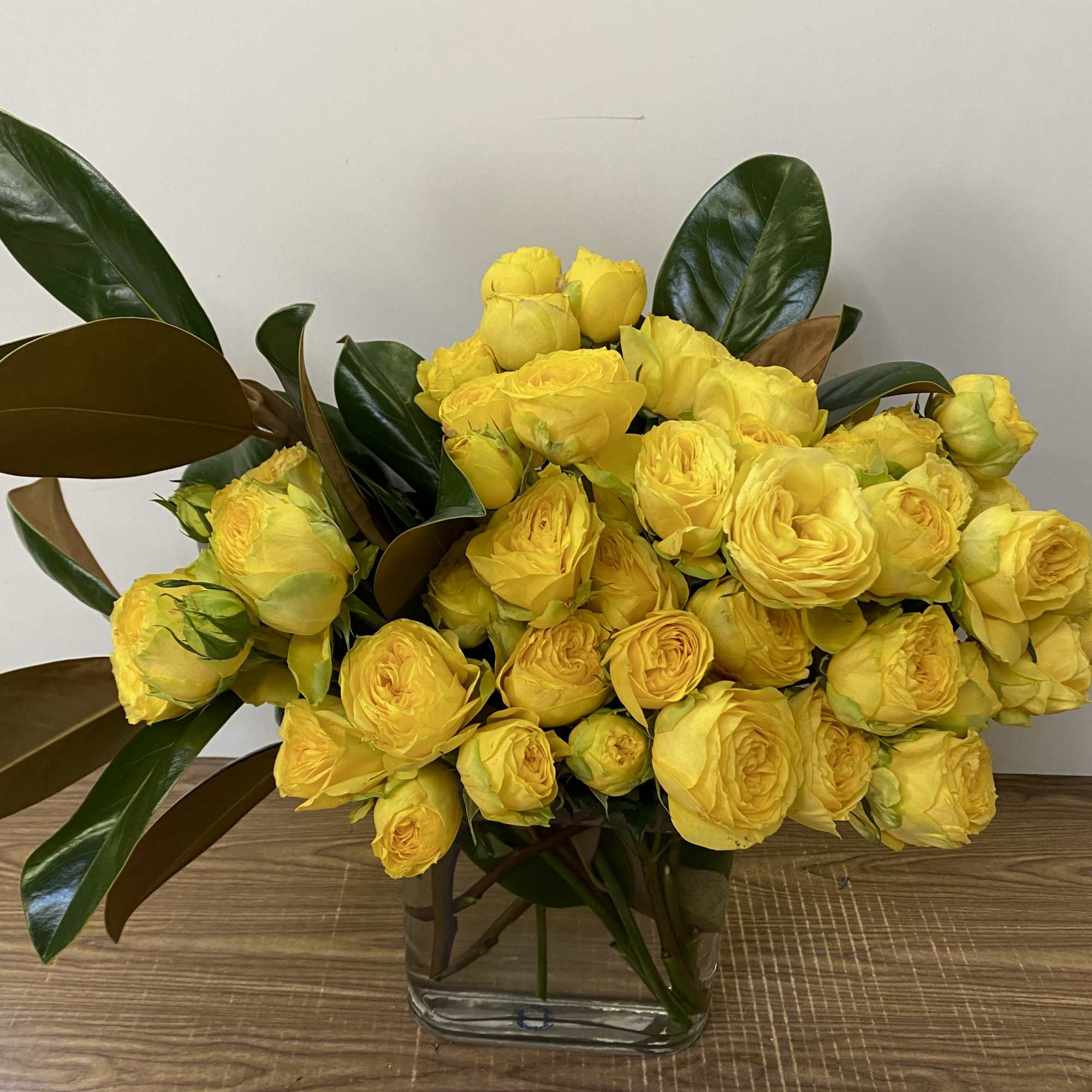 In a glass vase combination of Garden yellow roses with magnolia leaves
