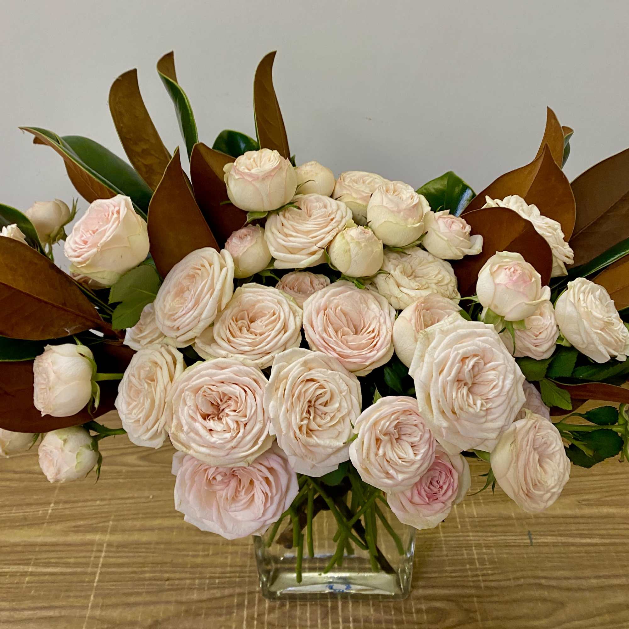 In a glass vase combination of Garden yellow roses with magnolia leaves