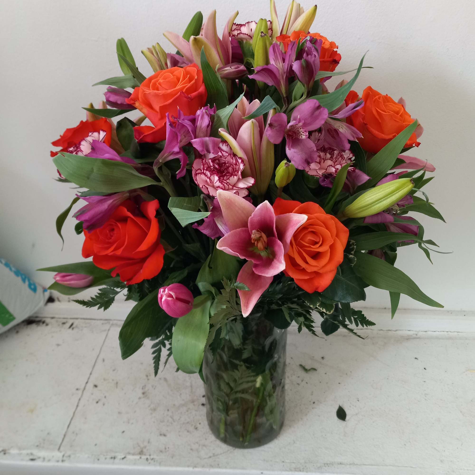 Beautiful orange roses mixed in with pink lilies, purple/pink alstroemeria and light