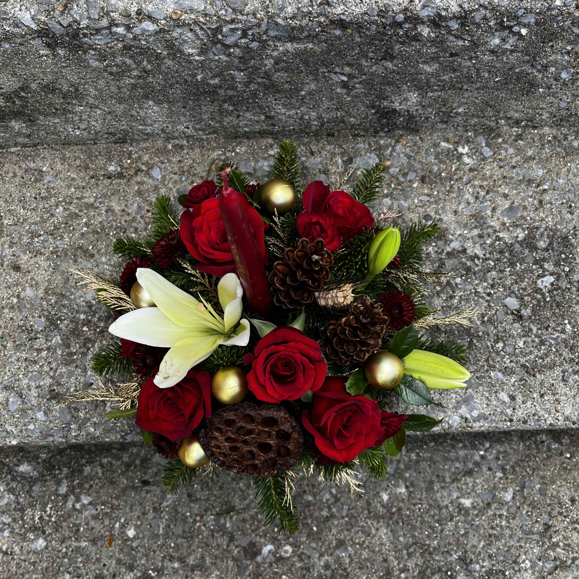 This arrangement has roses, lilies, Christmas ornaments, pinecones, mums , mini carns