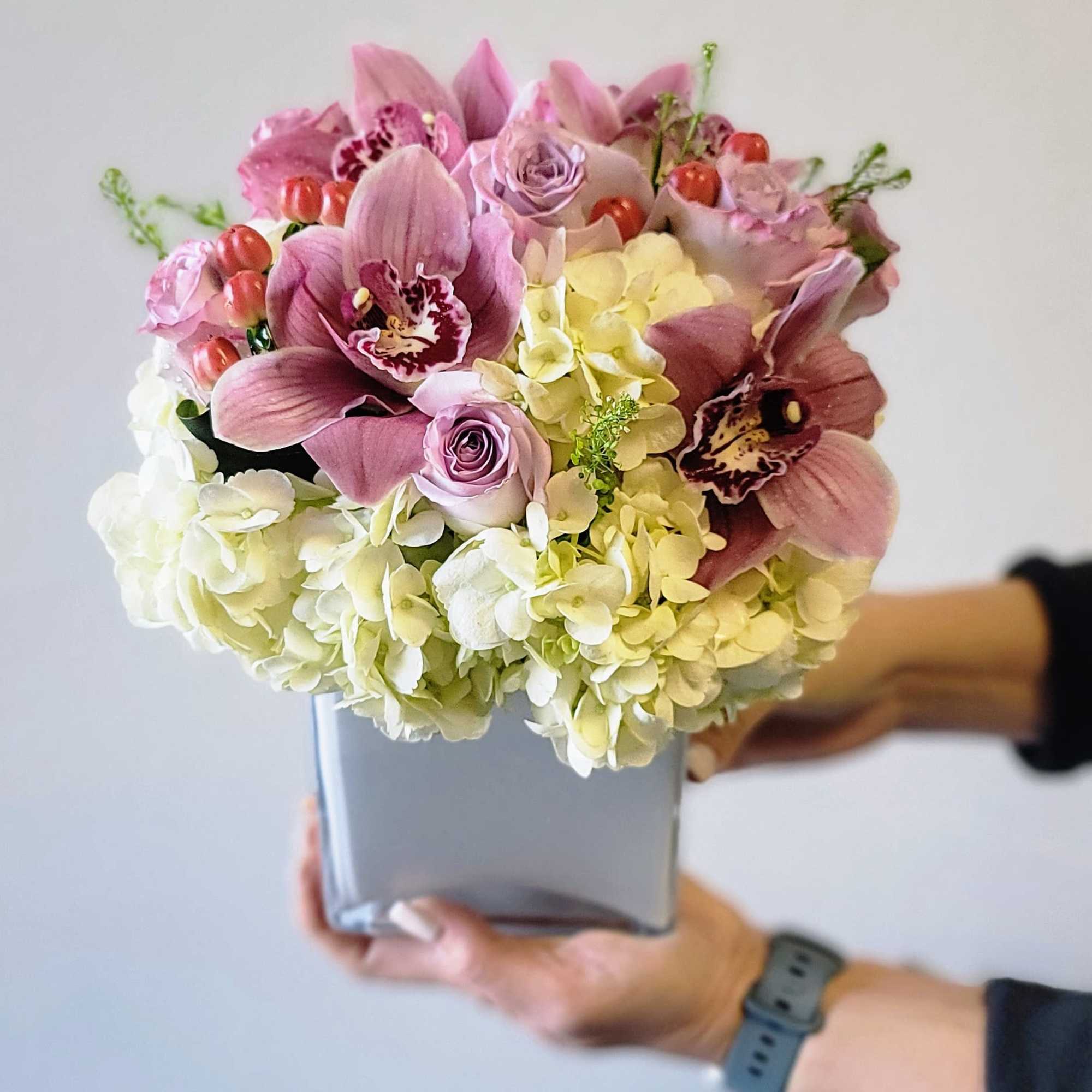 Featuring vibrant pink Cymbidium Orchids, soft lavender Roses, and white Hydrangeas, this