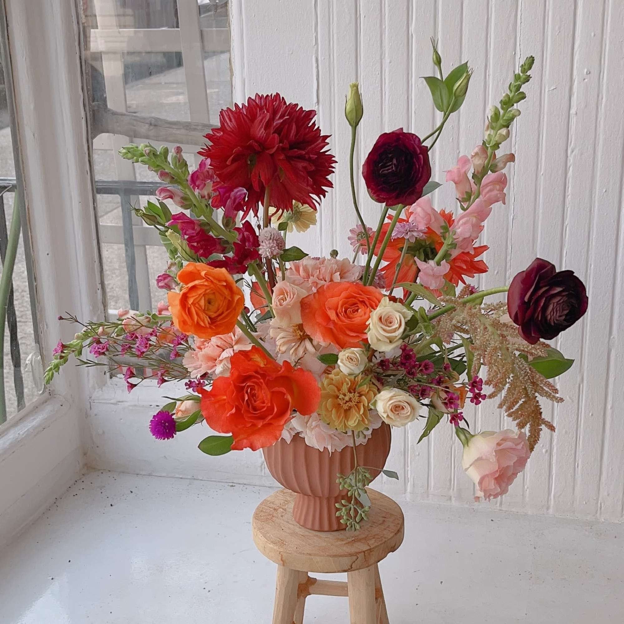 A vibrant fall arrangement featuring dahlias, roses, ranunculus, and mums in warm