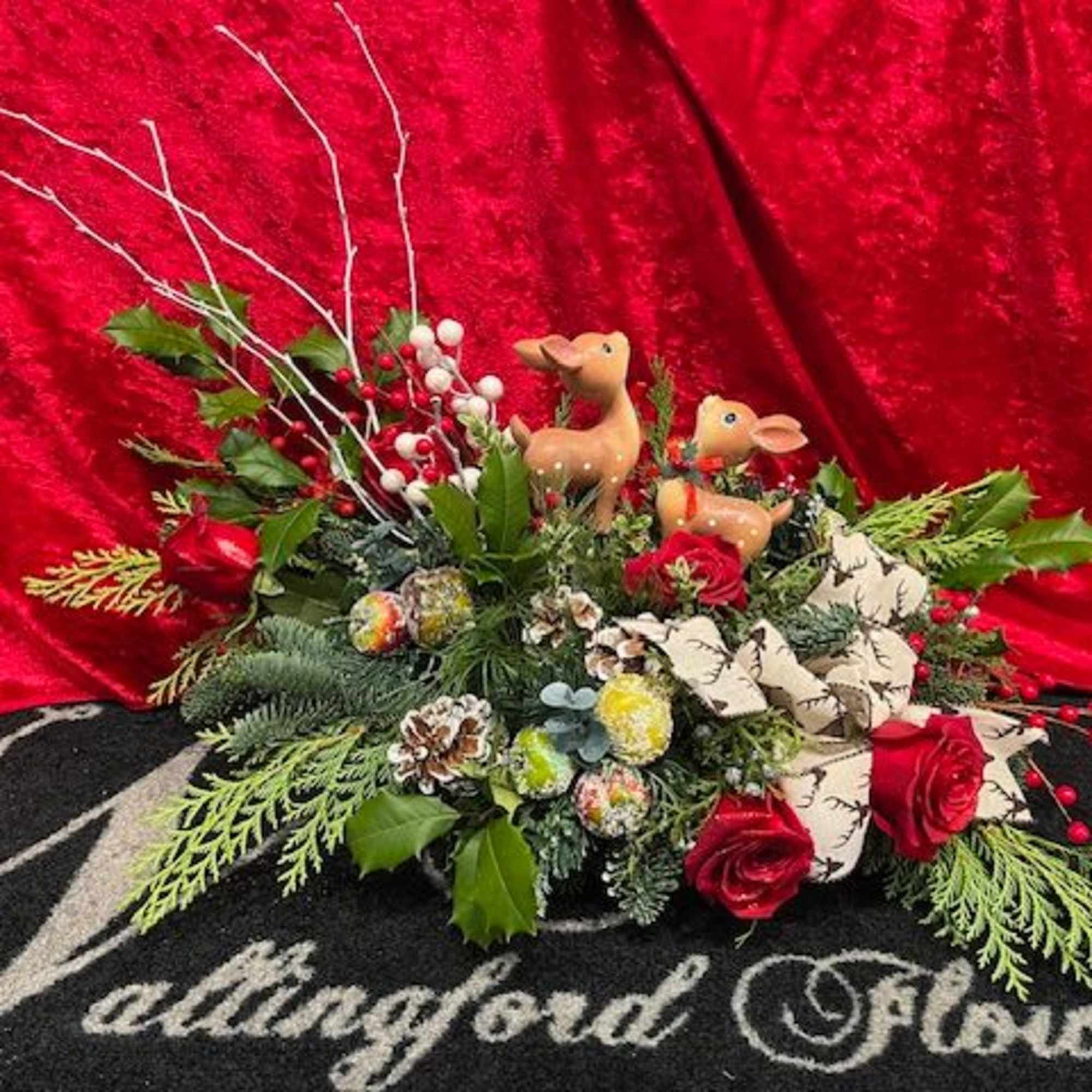 This design features two deer who are surrounded by winter greens, flowers