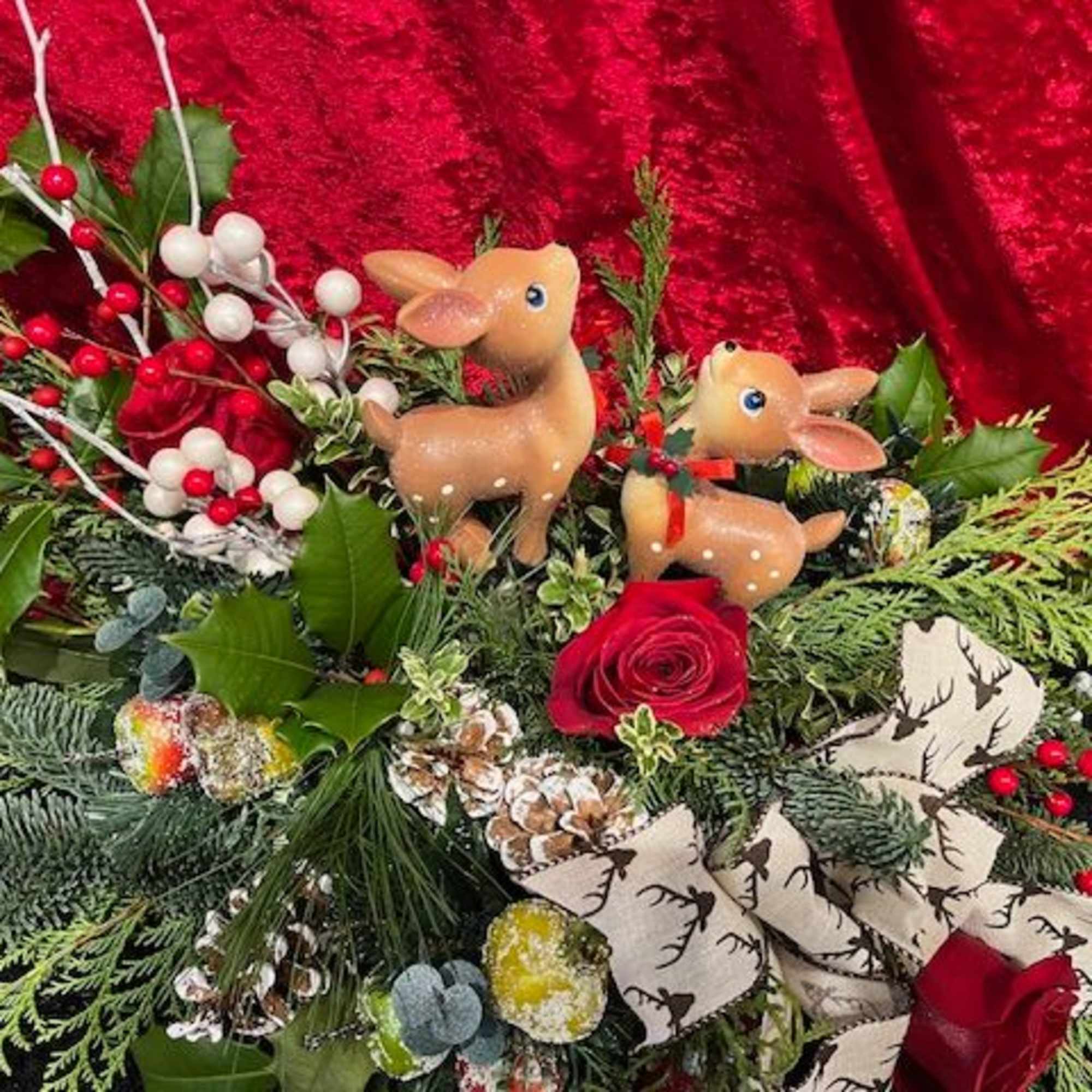 This design features two deer who are surrounded by winter greens, flowers