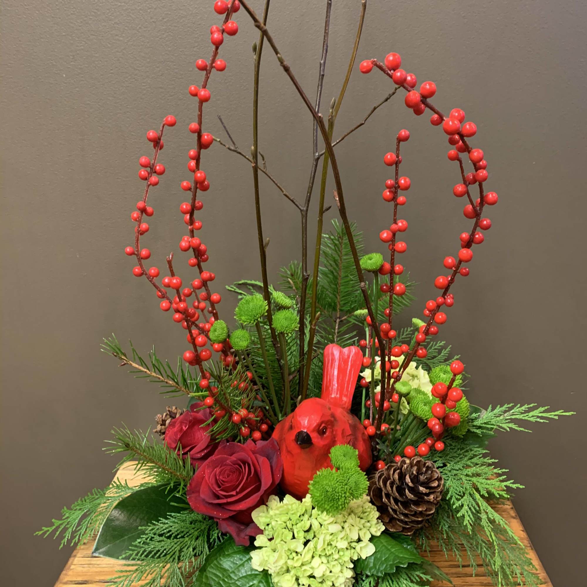 A beautiful cardinal nestled in an arrangement of red roses, green hydrangea