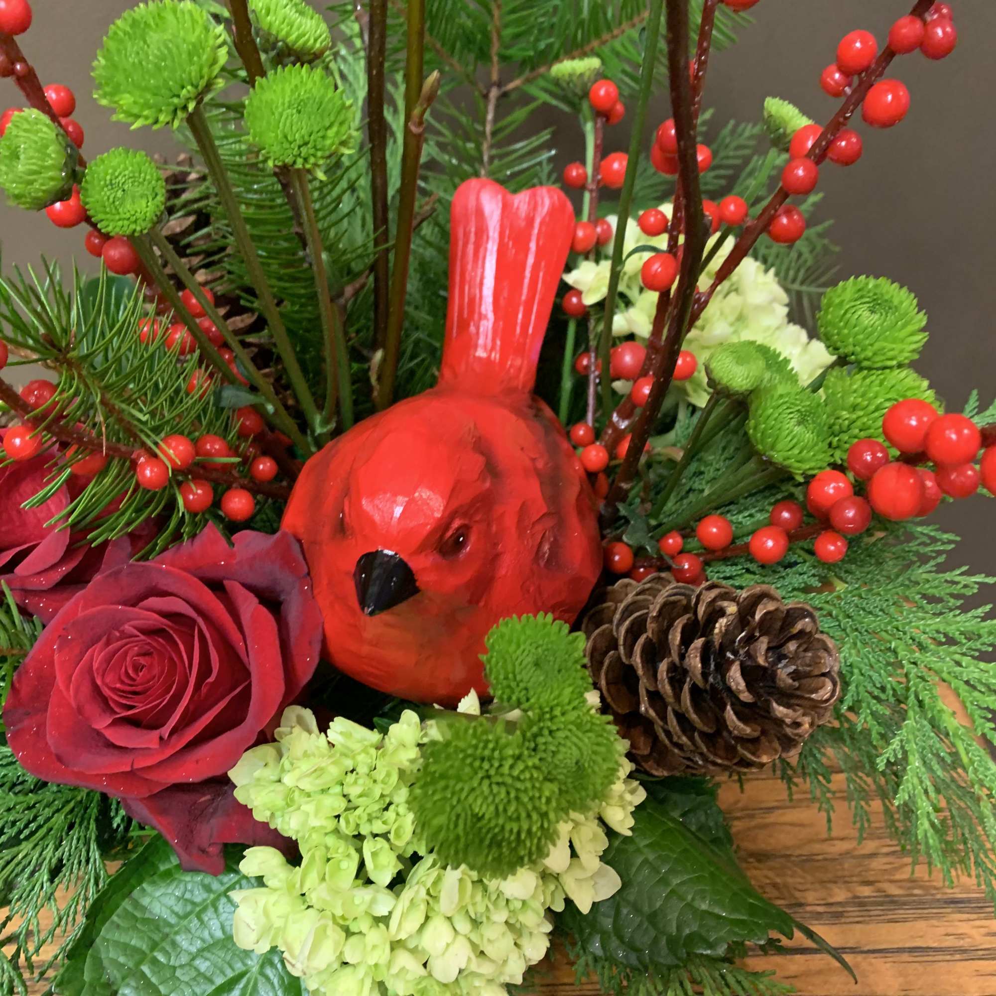 A beautiful cardinal nestled in an arrangement of red roses, green hydrangea