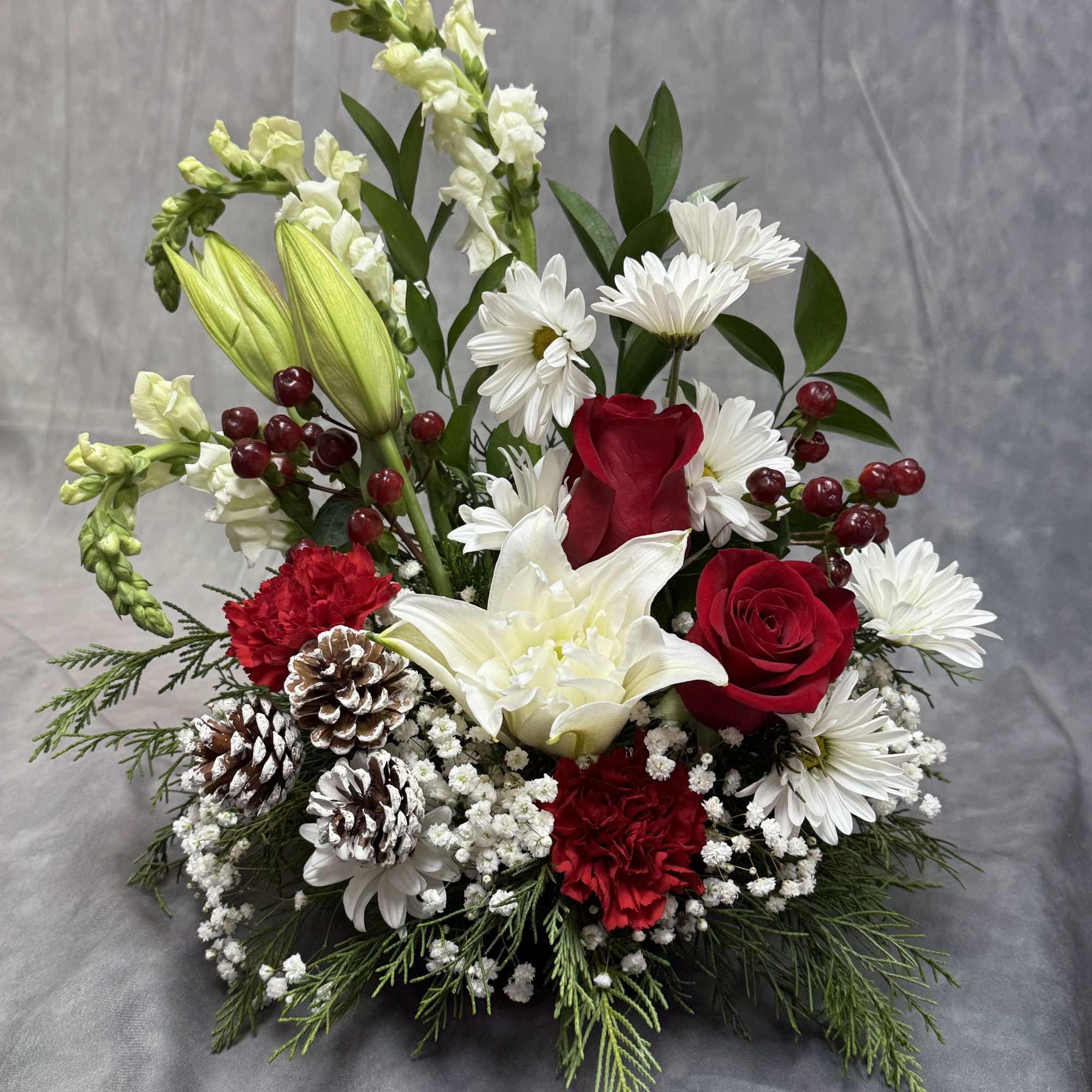 A festive Christmas arrangement featuring snowy pinecones, lush evergreens, red roses, white