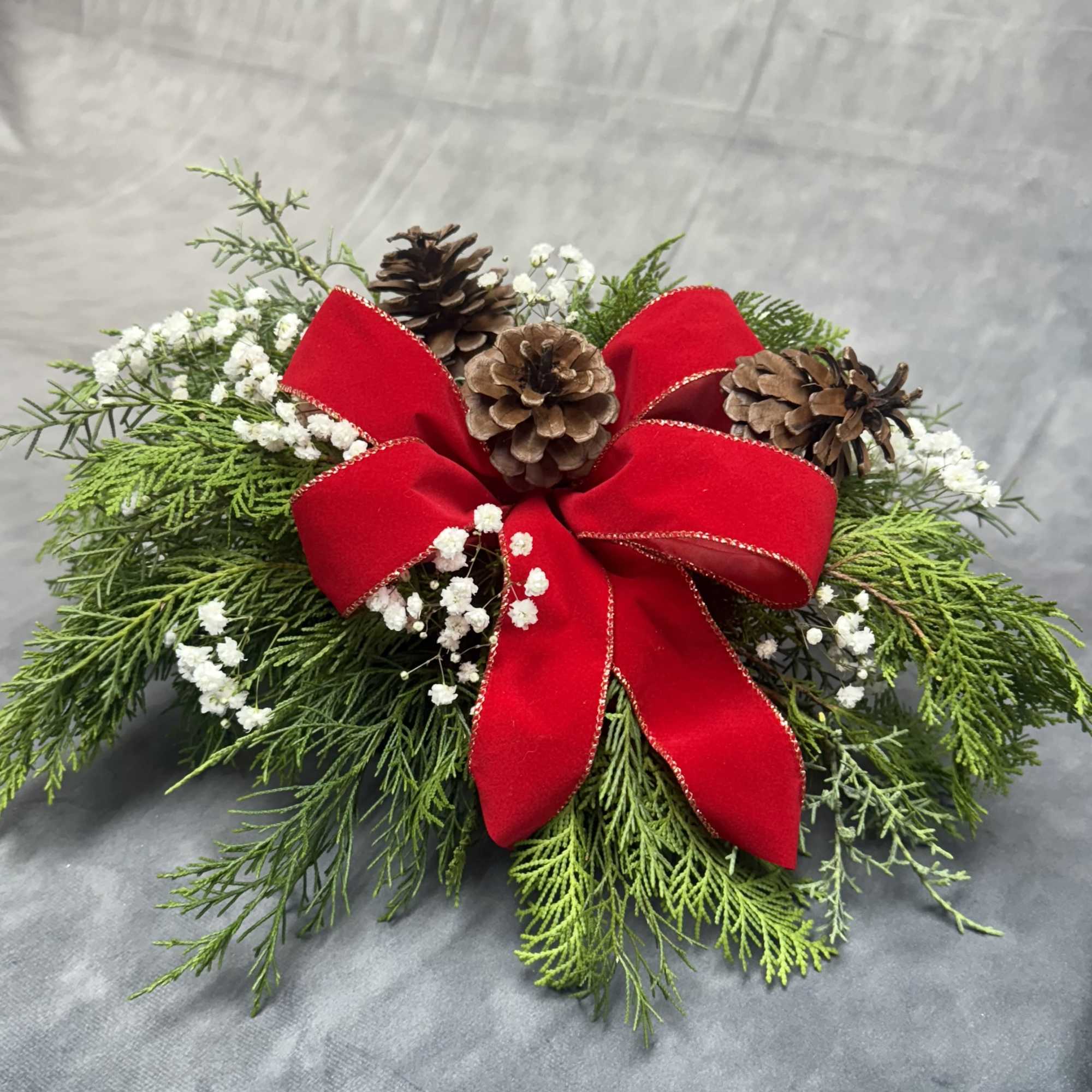 A fresh winter greenery centerpiece featuring lush evergreens, natural pinecones, soft baby&rsquo;s