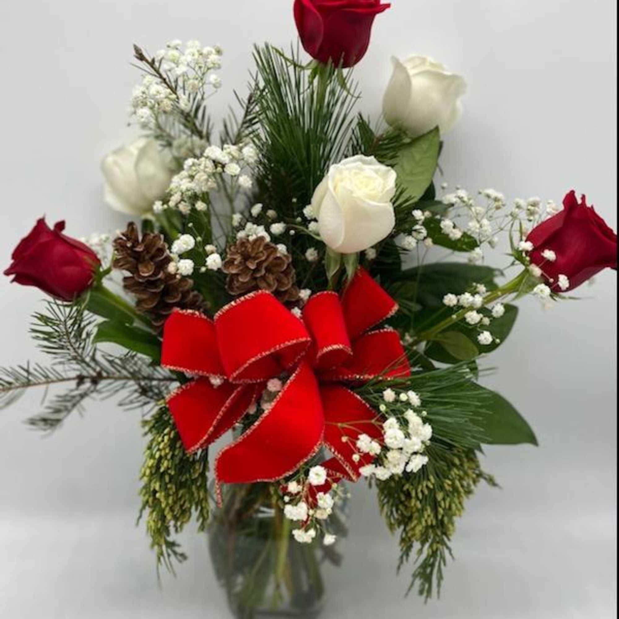 A clear vase of red &amp; white roses mixed amongst Christmas Greens