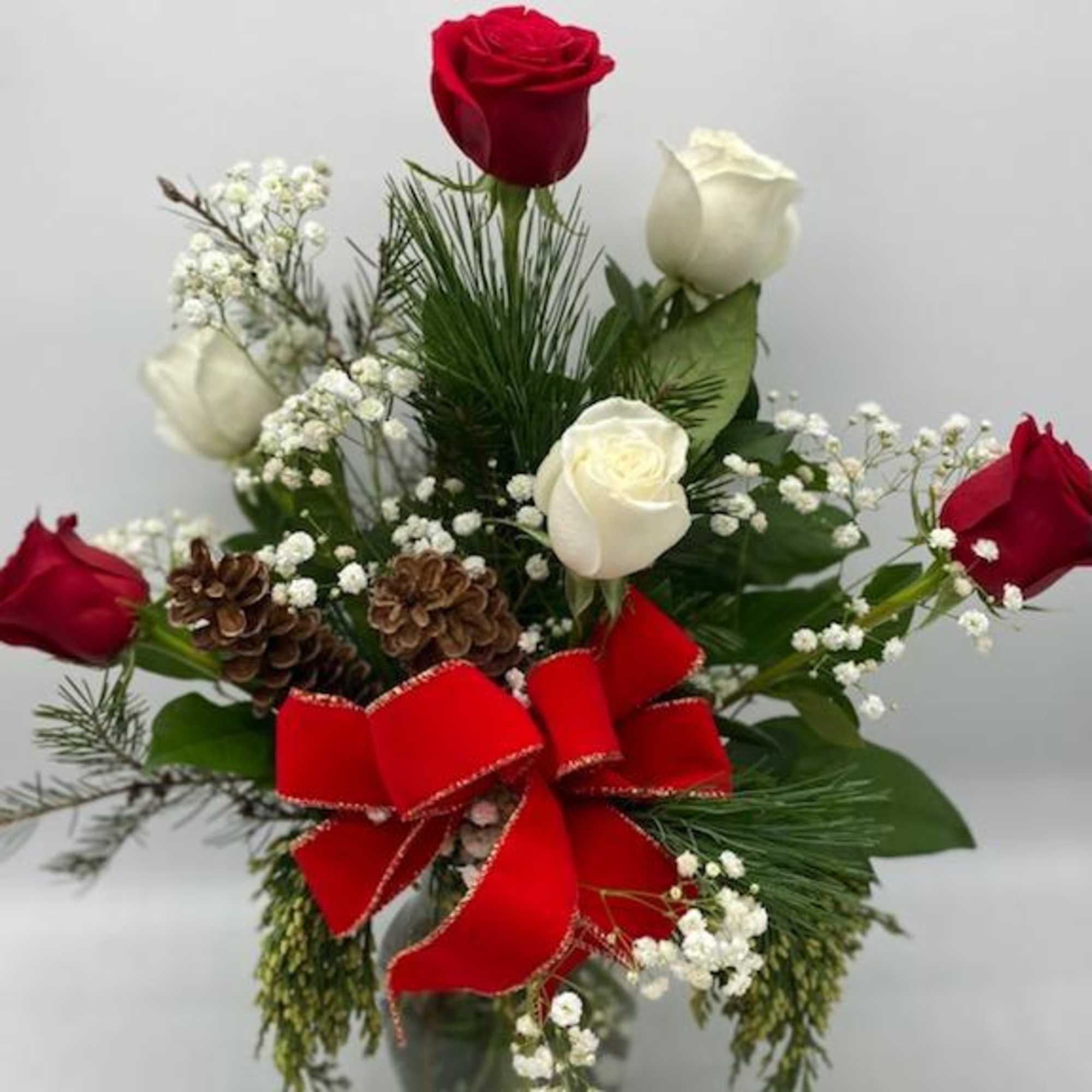 A clear vase of red &amp; white roses mixed amongst Christmas Greens