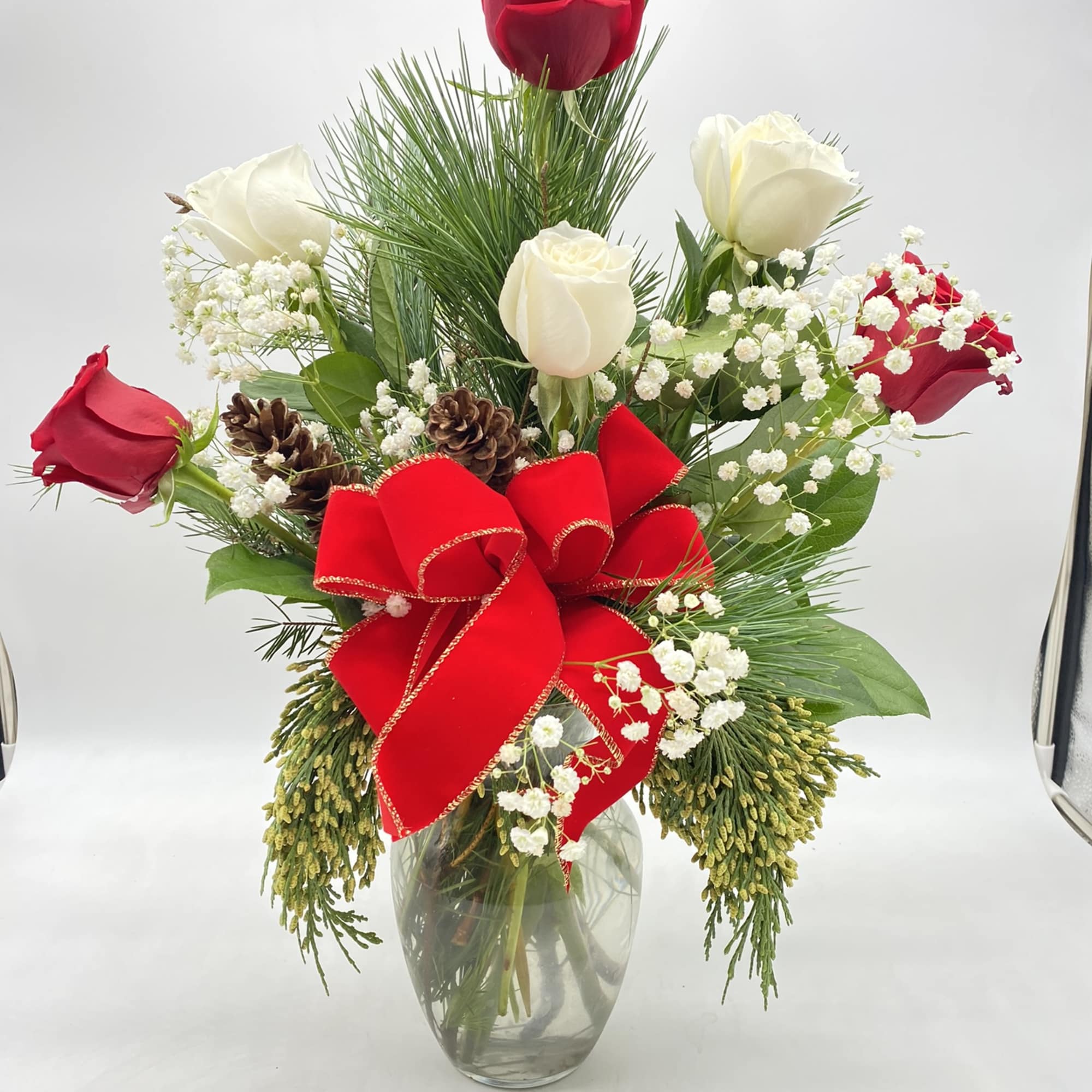 A clear vase of red &amp; white roses mixed amongst Christmas Greens