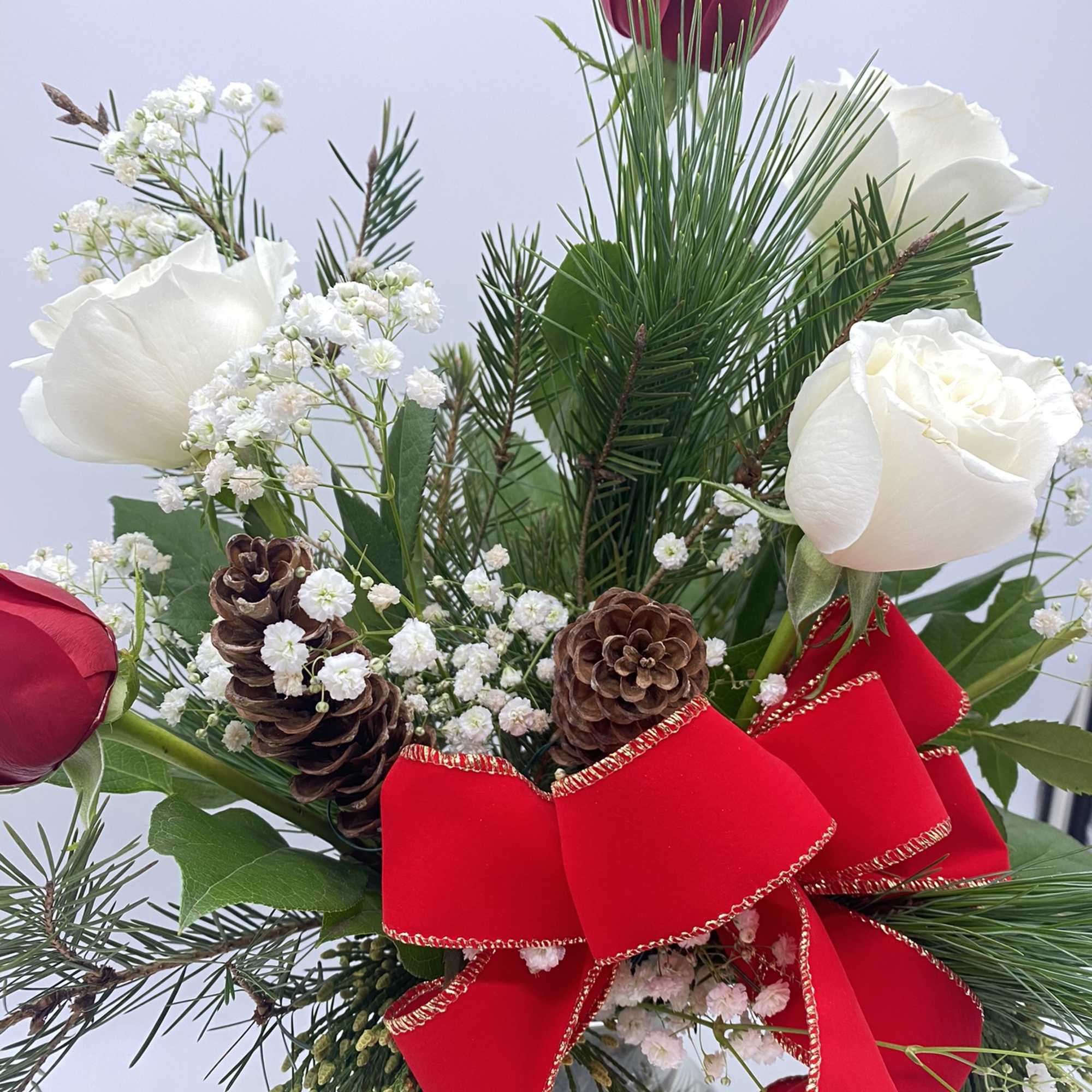 A clear vase of red &amp; white roses mixed amongst Christmas Greens