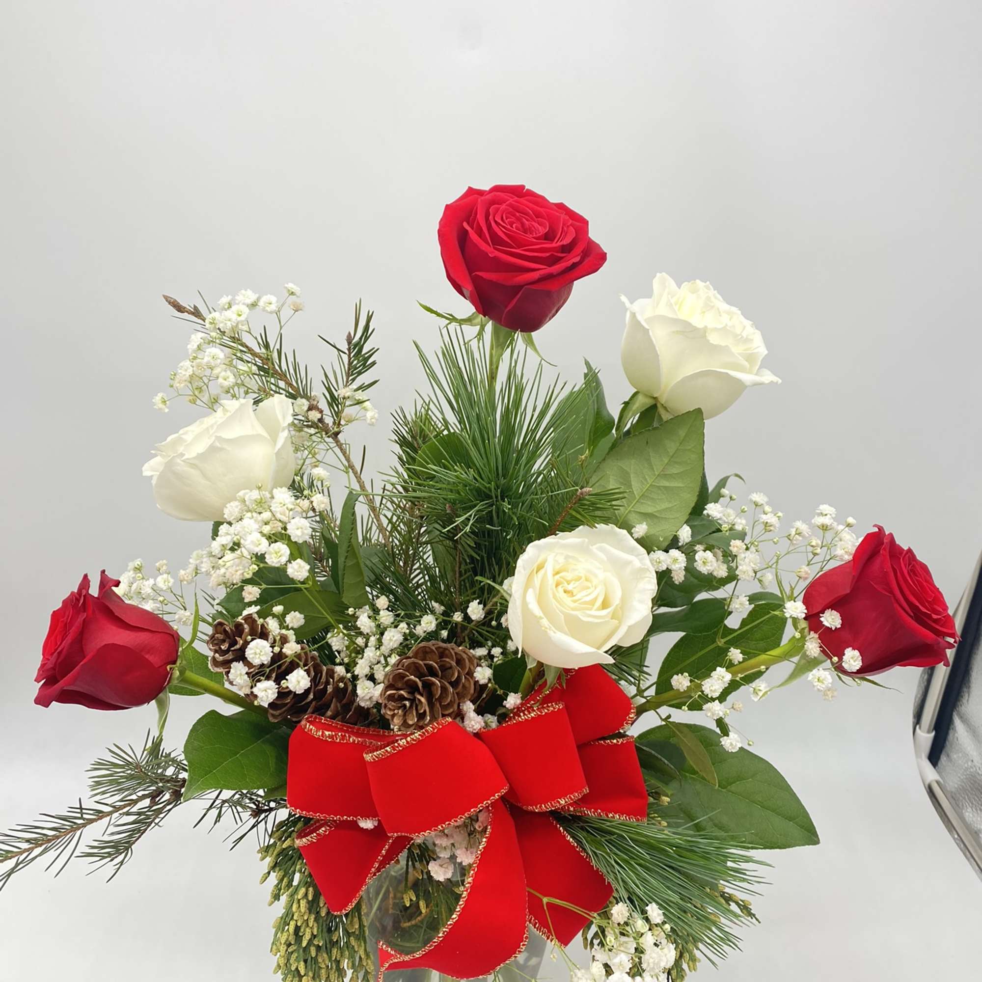 A clear vase of red &amp; white roses mixed amongst Christmas Greens