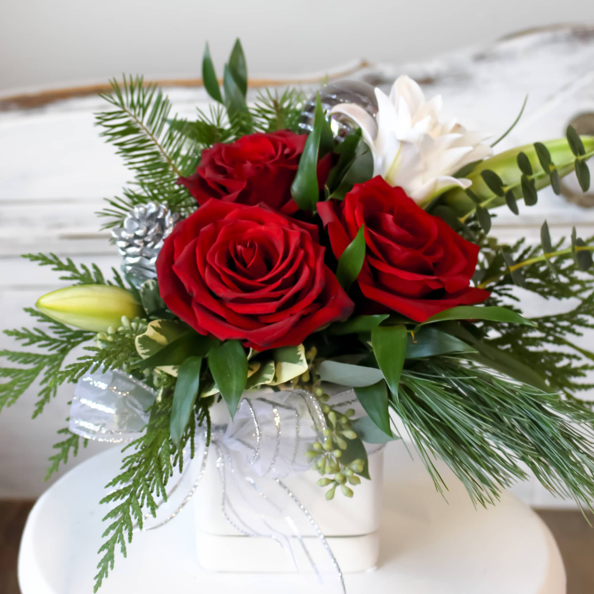 This holiday arrangement includes, red roses, lilies, holiday greens and accents. 