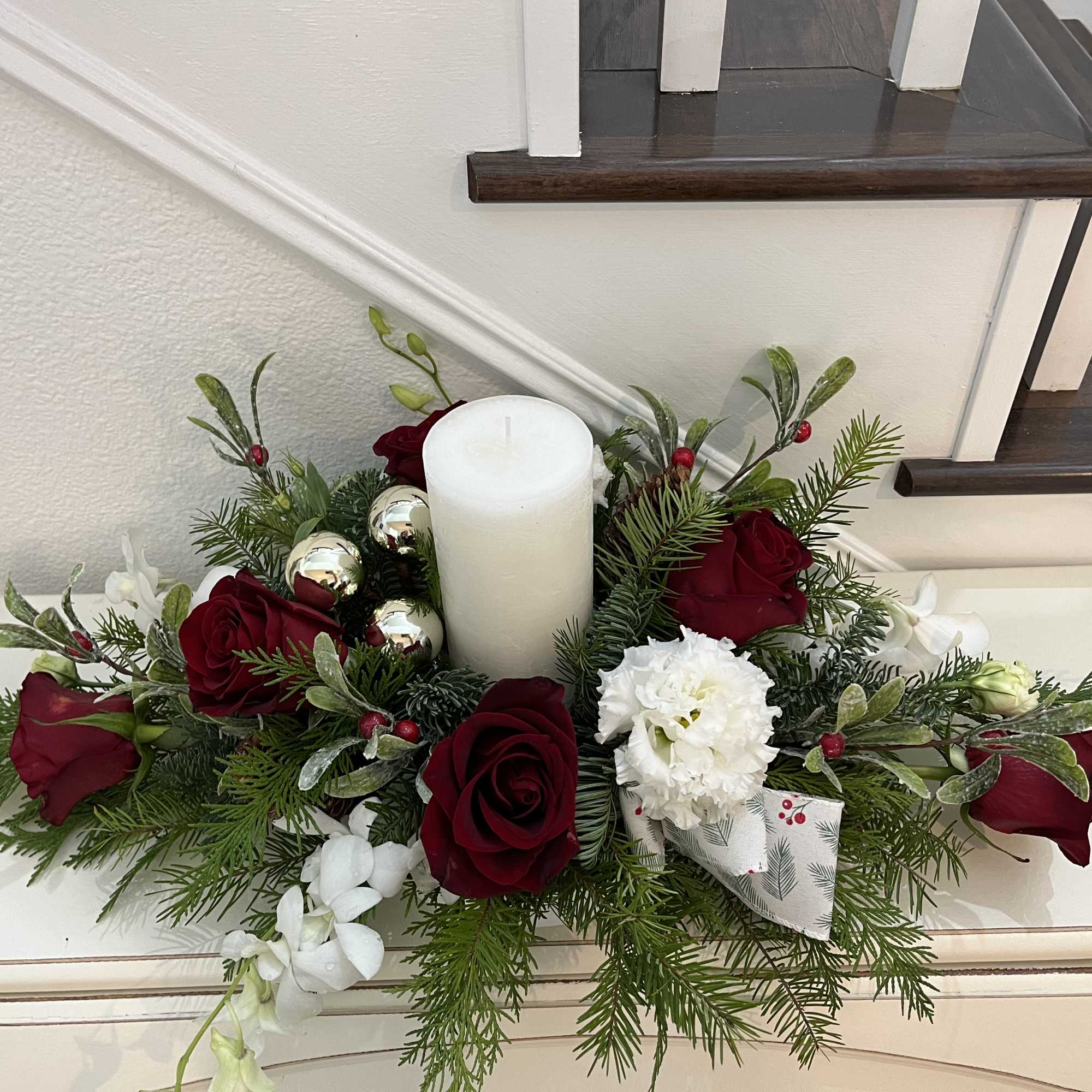 Candle arrangement with Christmas greens, roses, lisianthus 
, dendrobium orchids, gold bulbs