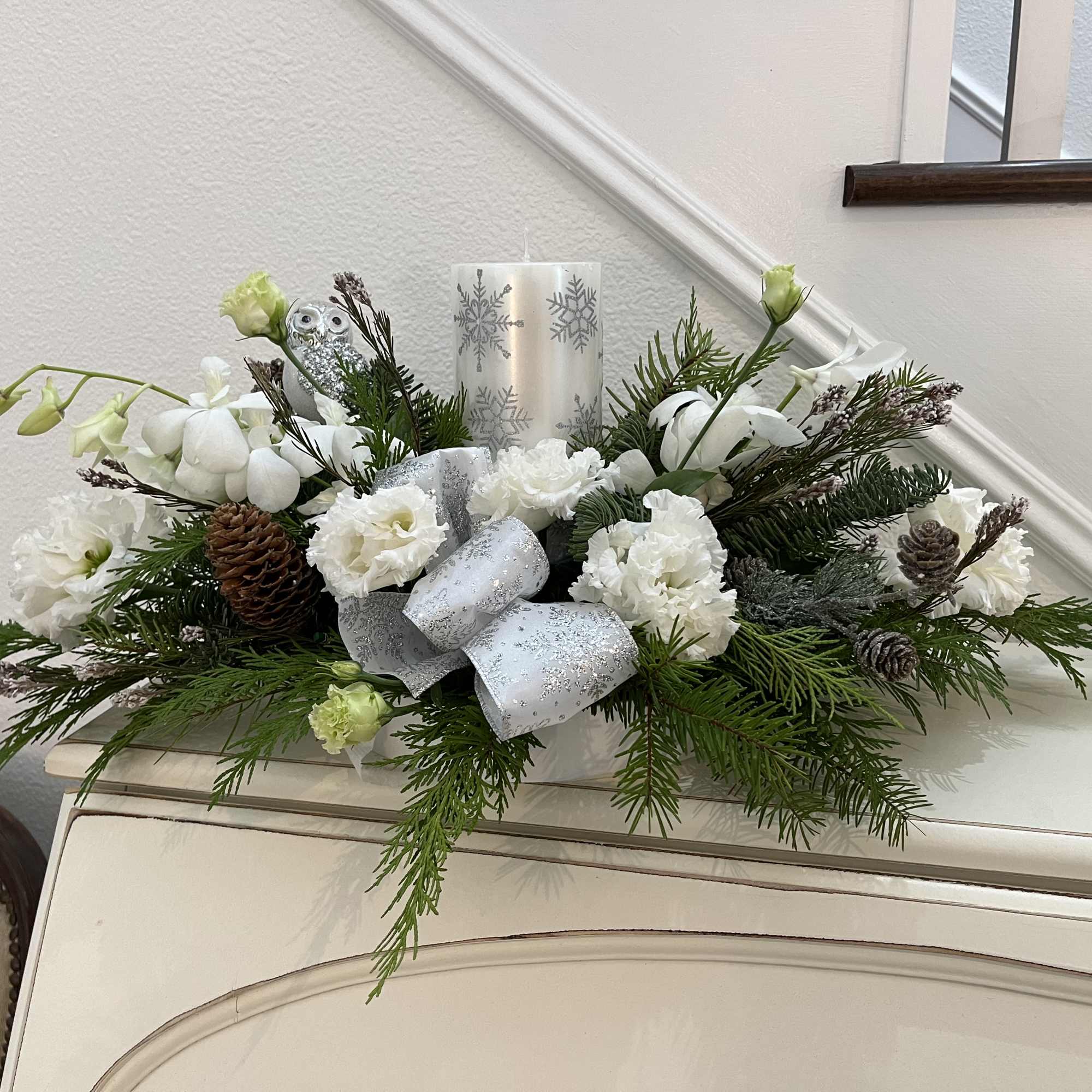 Christmas greens, orchids, lisianthus, candle, ribbons, and pine cones, with candle and